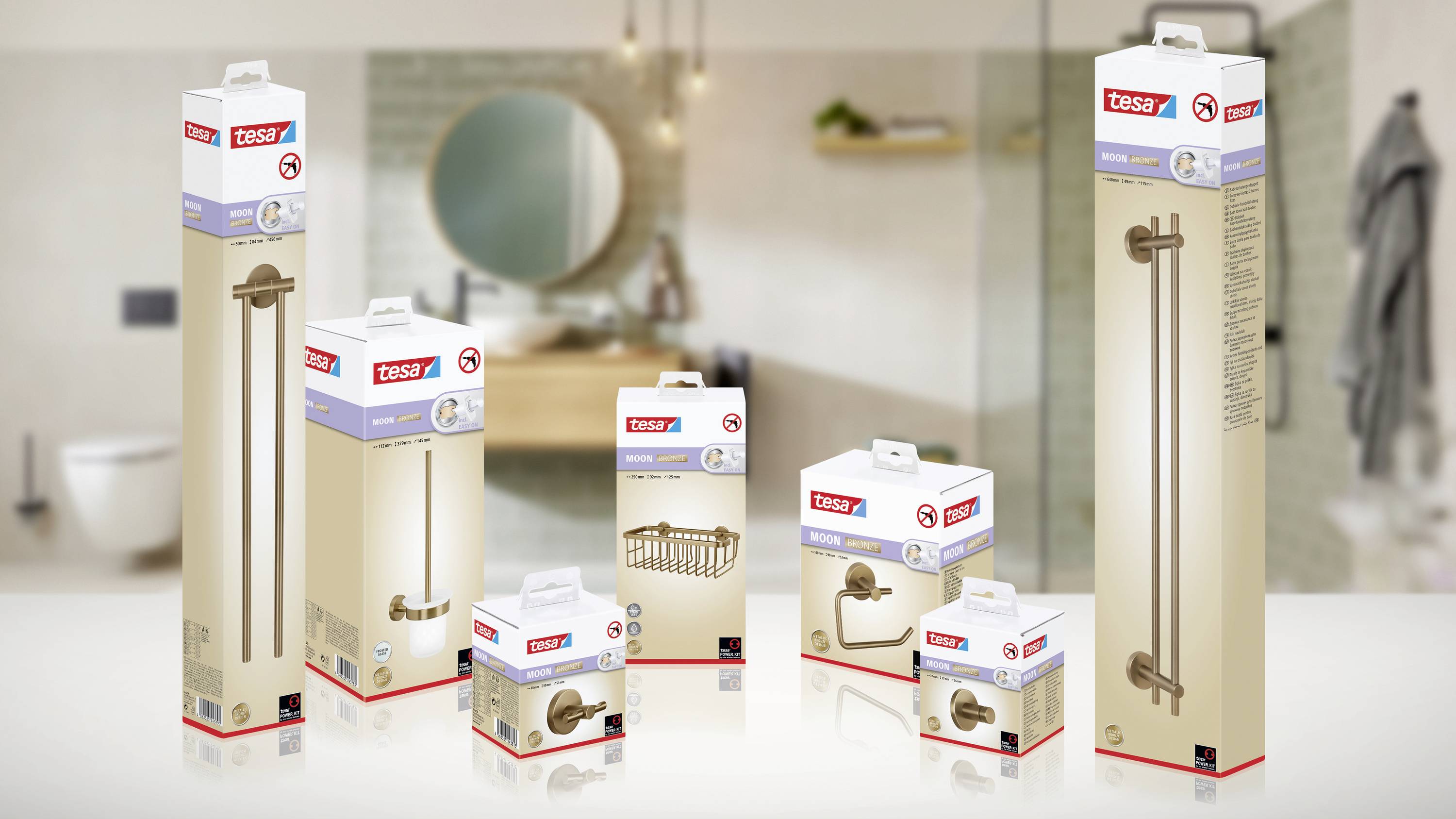 Verschiedene Verpackungen von Tesa-Produkten für Badezimmeranwendungen, wie Duschgriffe und Handtuchhalter, sind auf einem Tisch arrangiert. Im Hintergrund ist ein unscharfes Badezimmer zu sehen.