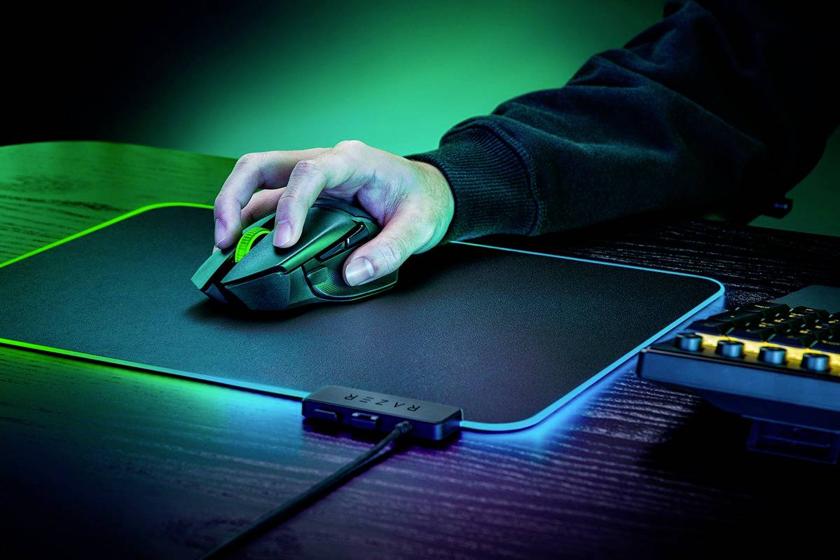 Eine Person bedient eine Computermaus auf einem leuchtenden RGB-Mauspad, daneben eine Tastatur mit gelber Hintergrundbeleuchtung.