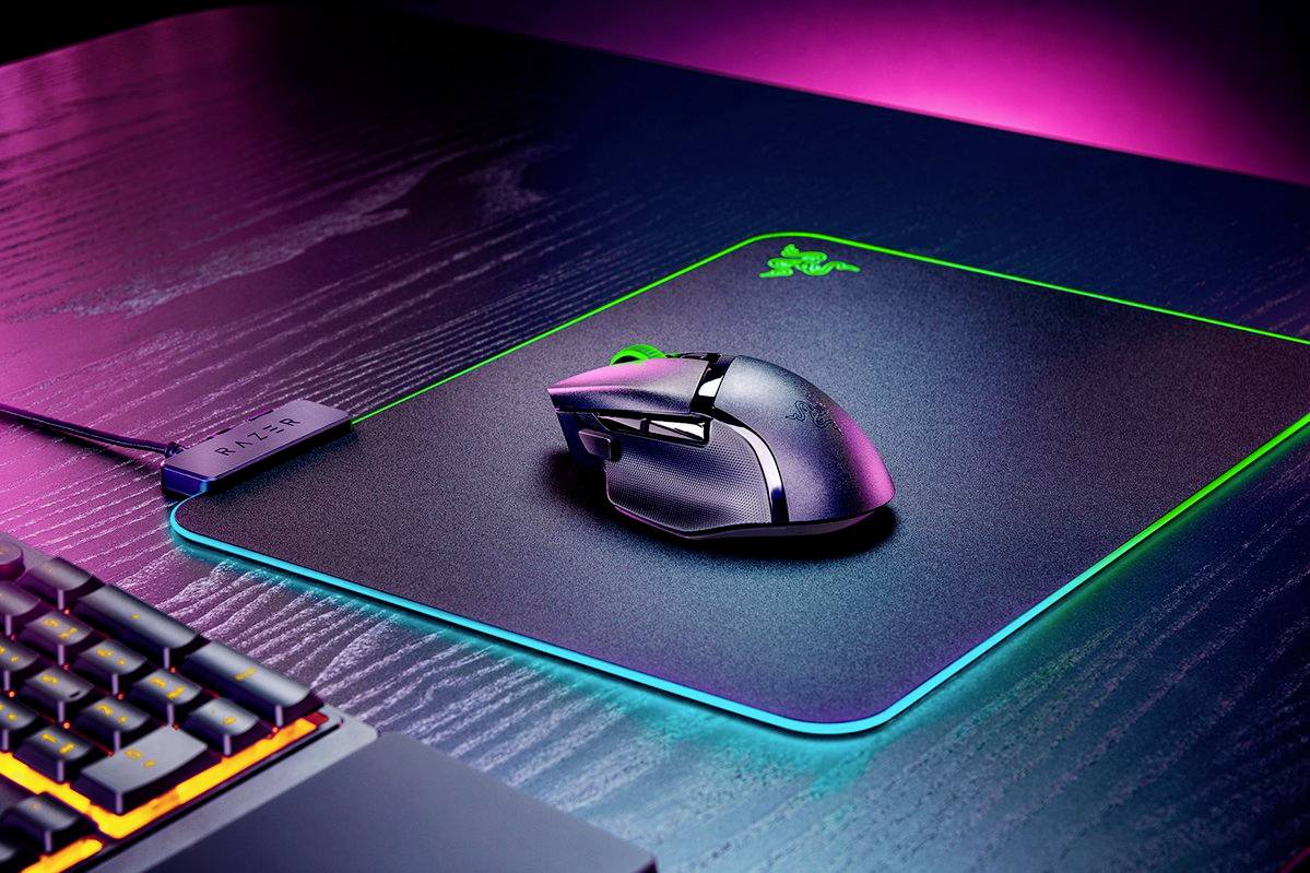 Eine Gaming-Maus und -Tastatur auf einem beleuchteten Schreibtisch in Neonfarben. Die Maus liegt auf einem Mauspad mit leuchtendem Rand.