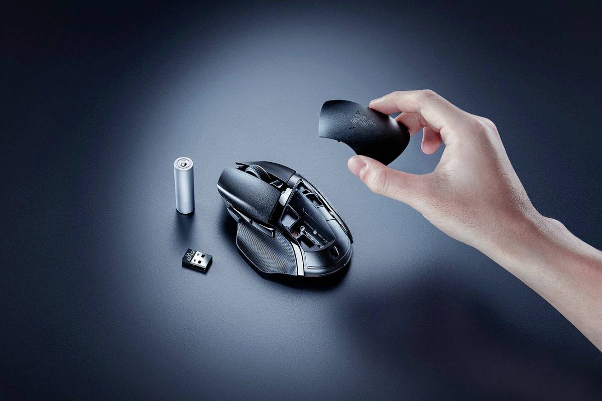 'Hand legt Oberschale auf eine Gaming-Maus,' daneben Batterie und USB-Dongle. Fokus auf benutzerfreundliches Design und Zubehör.