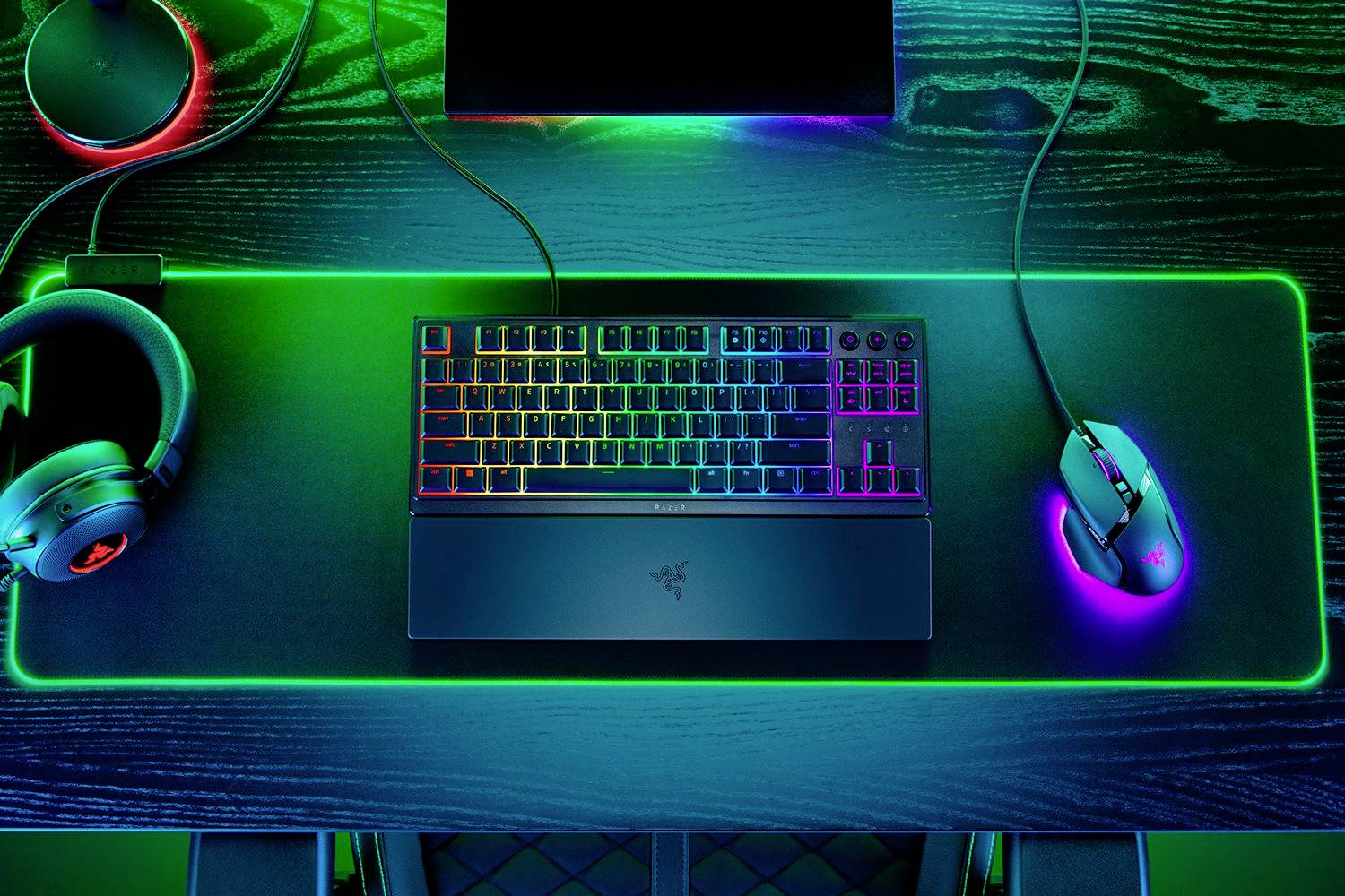 Gaming-Setup mit RGB-beleuchteter Tastatur und Maus auf einem leuchtenden Mauspad. Ein Headset liegt links daneben auf dem Schreibtisch.