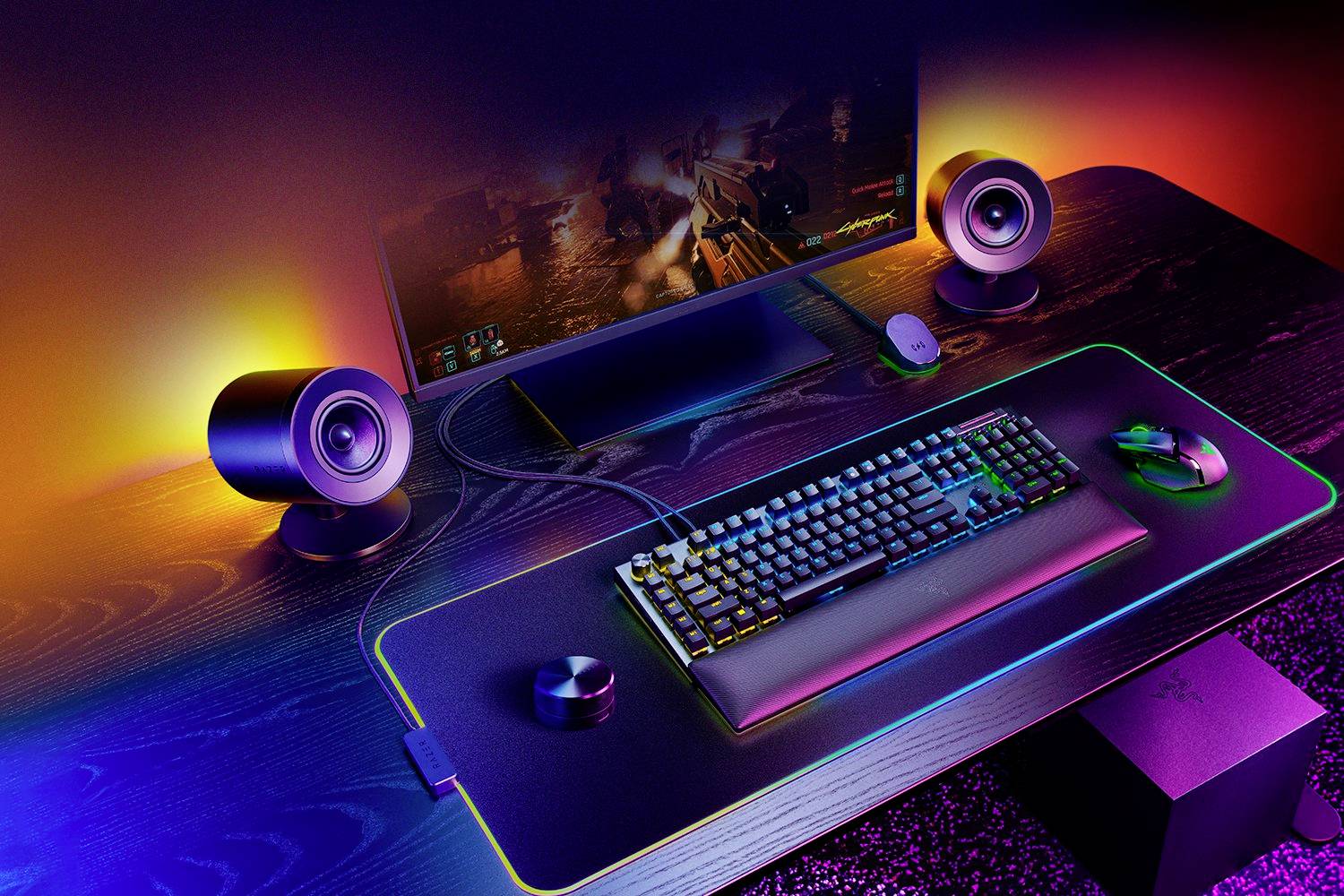 Ein stilvoller Schreibtisch mit beleuchteter Gaming-Tastatur, Maus, Lautsprechern und Monitor, der ein Videospiel zeigt.