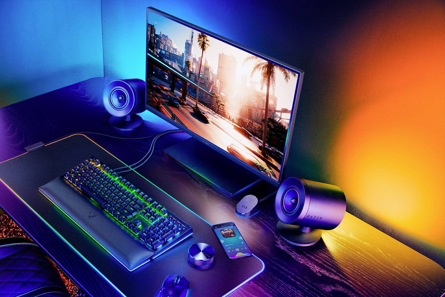 Ein farbenfroher Gaming-Setup mit Monitor, Tastatur, Maus und Lautsprechern auf einem Tisch. Der Bildschirm zeigt eine Stadtansicht.