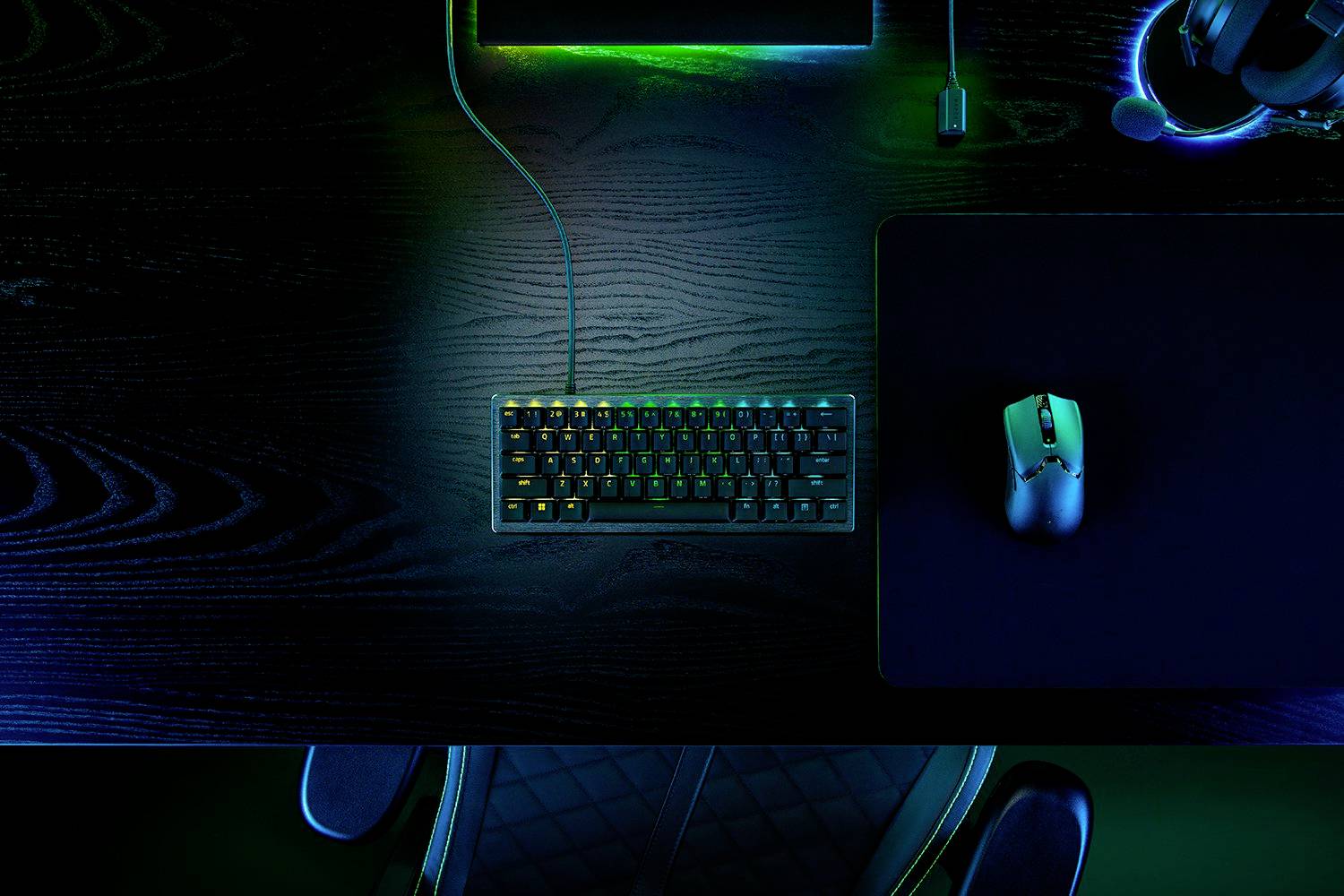 Eine beleuchtete Tastatur und Gaming-Maus auf einem Schreibtisch mit dunkler Oberfläche, umgeben von schwachem, farbigem Licht.