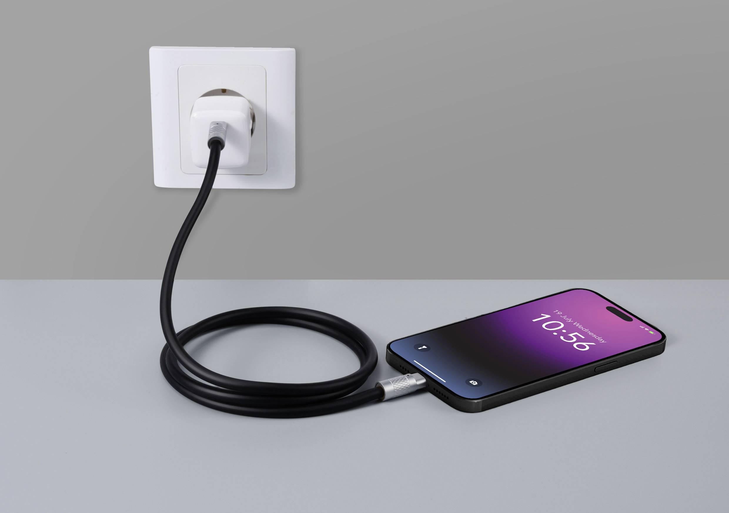 Smartphone mit Ladebildschirm liegt auf einem Tisch und ist über ein schwarzes Kabel mit einer Wandsteckdose verbunden.