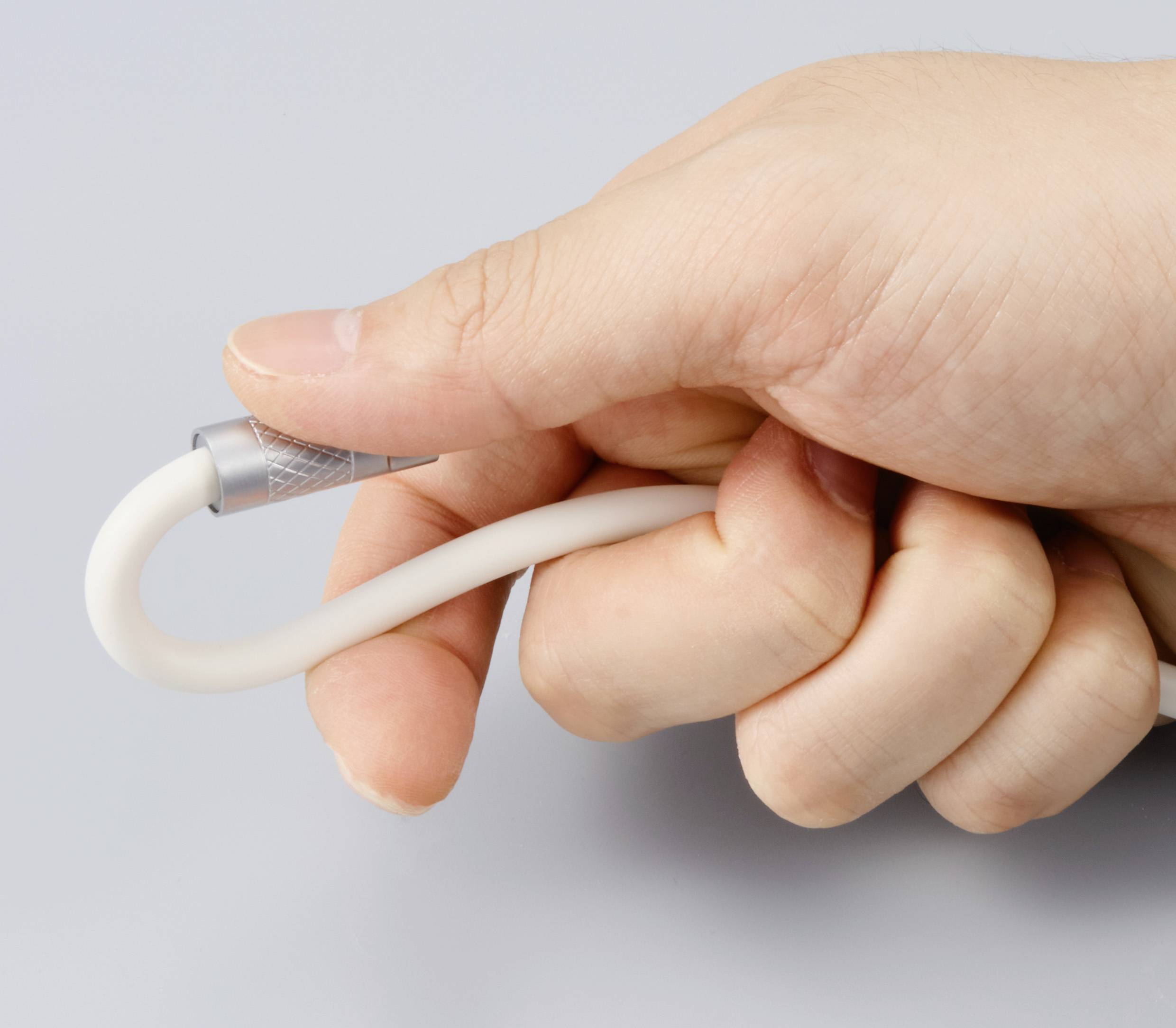 Eine Hand hält ein gebogenes, weißes Kabel mit silbernem Anschluss, möglicherweise ein Daten- oder Ladekabel, vor grauem Hintergrund.