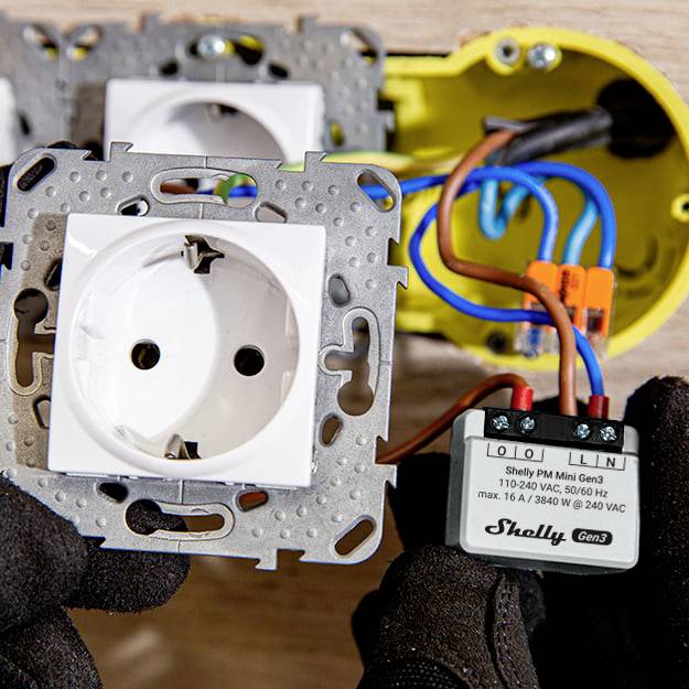 Zwei Steckdosenmodule und ein offenes Gehäuse mit einem Shelly PM Mini Gen3. Eine Person hält das Modul und bereitet die Installation vor.