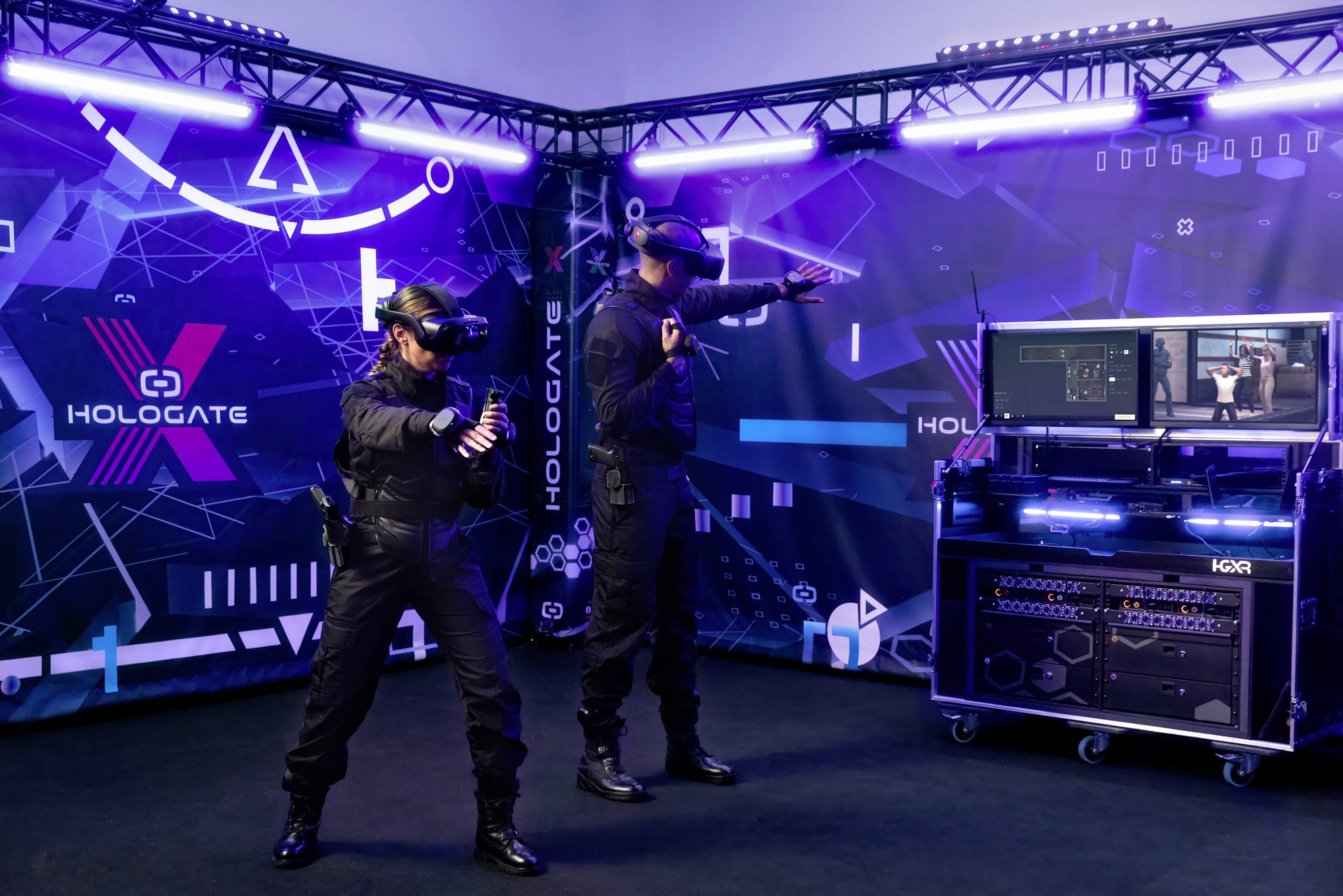 Zwei Personen in schwarzer Kleidung tragen VR-Brillen und befinden sich in einem Raum mit Hologate Logo und Technologie-Setup.