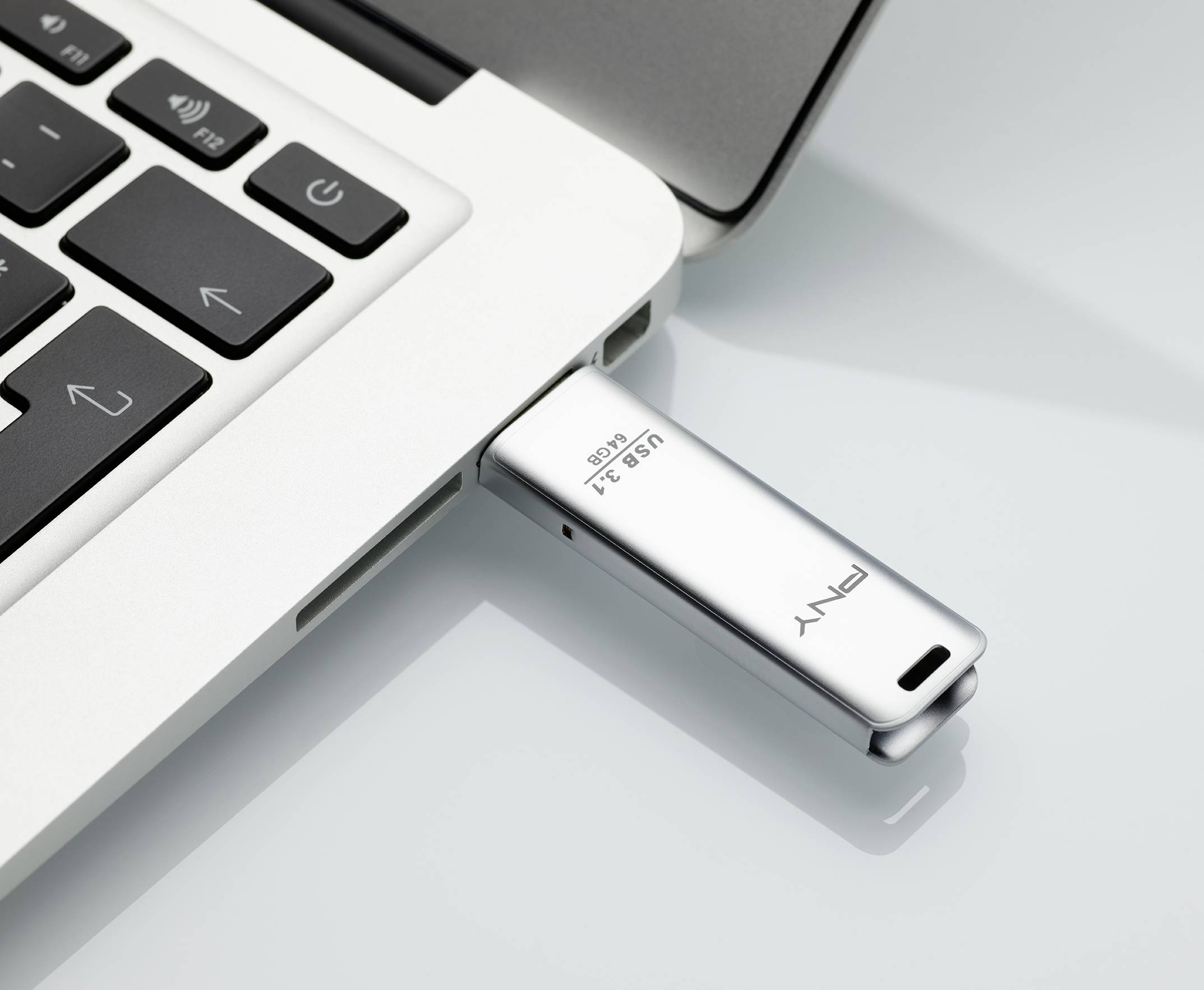 Ein Laptop mit einer silbernen USB-Stick, beschriftet mit 'USB 3.1', eingesteckt. Der Laptop liegt auf einer glatten Oberfläche.