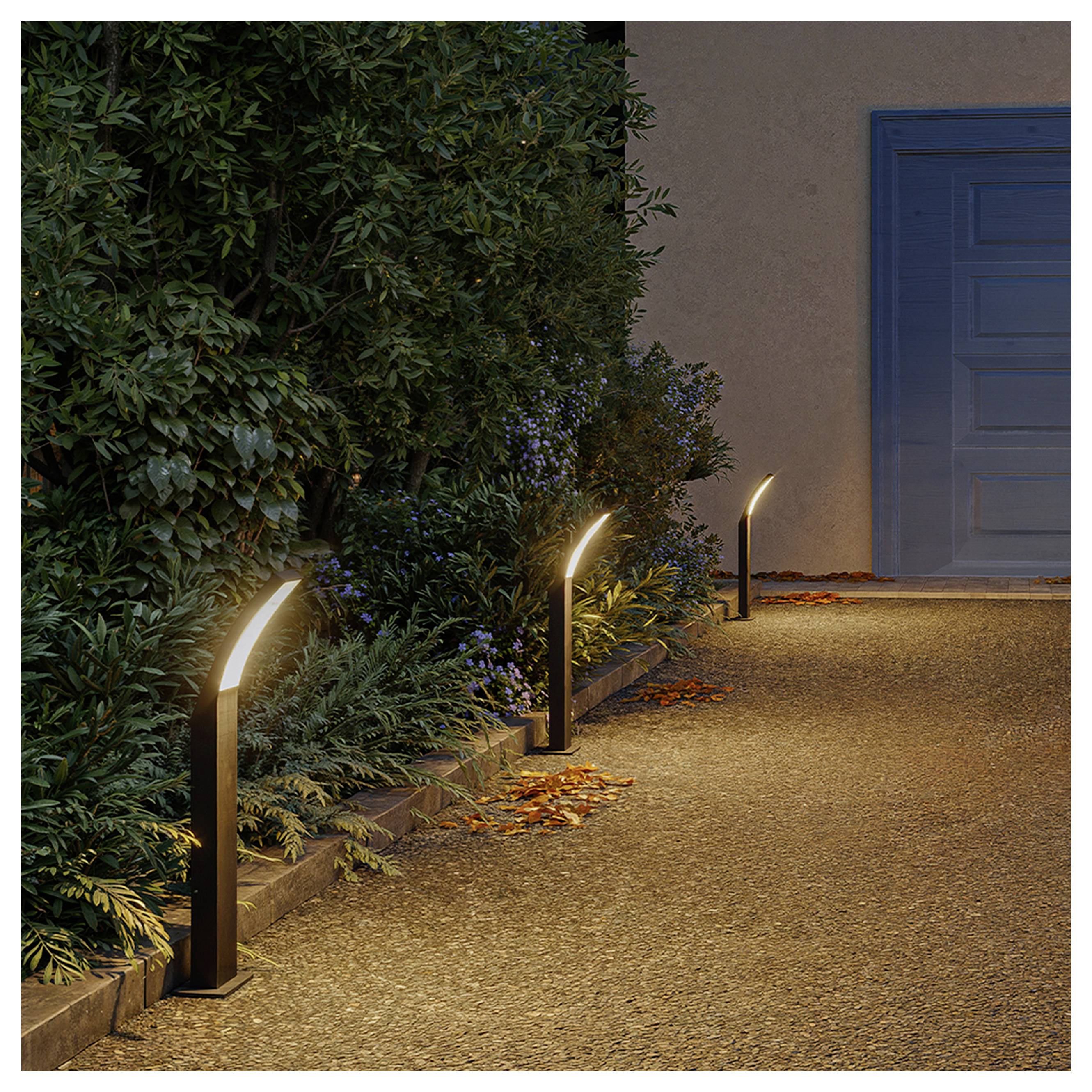 Drei moderne Wegeleuchten beleuchten einen Gartenweg neben dichten Sträuchern und führen zur Dämmerung auf eine blaue Tür zu.
