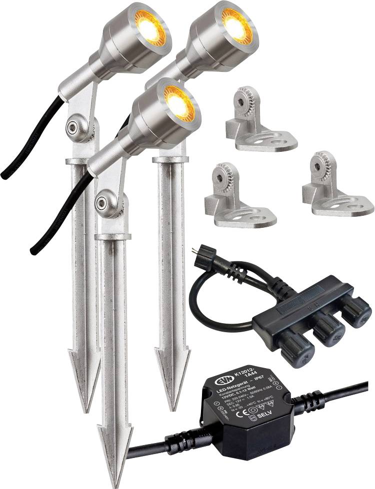 Drei verstellbare Scheinwerfer auf Bodenpfosten mit Montageklammern, Außenstromverteiler und Transformator für ein Landschaftsbeleuchtungsset.