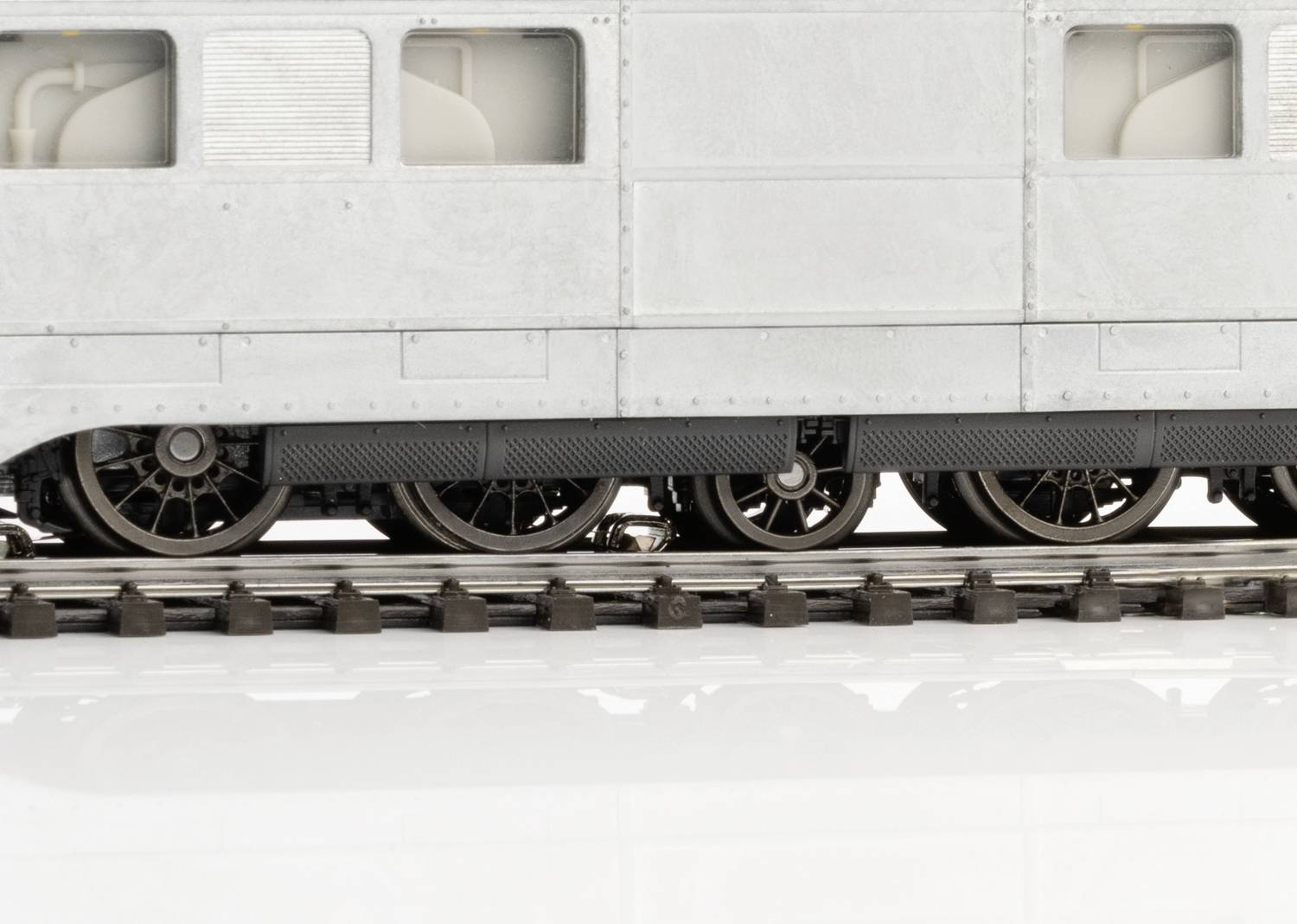 Nahaufnahme eines Modelleisenbahnwagens mit Sicht auf die Räder und Schienen. Der Wagen ist grau und zeigt feine Details.