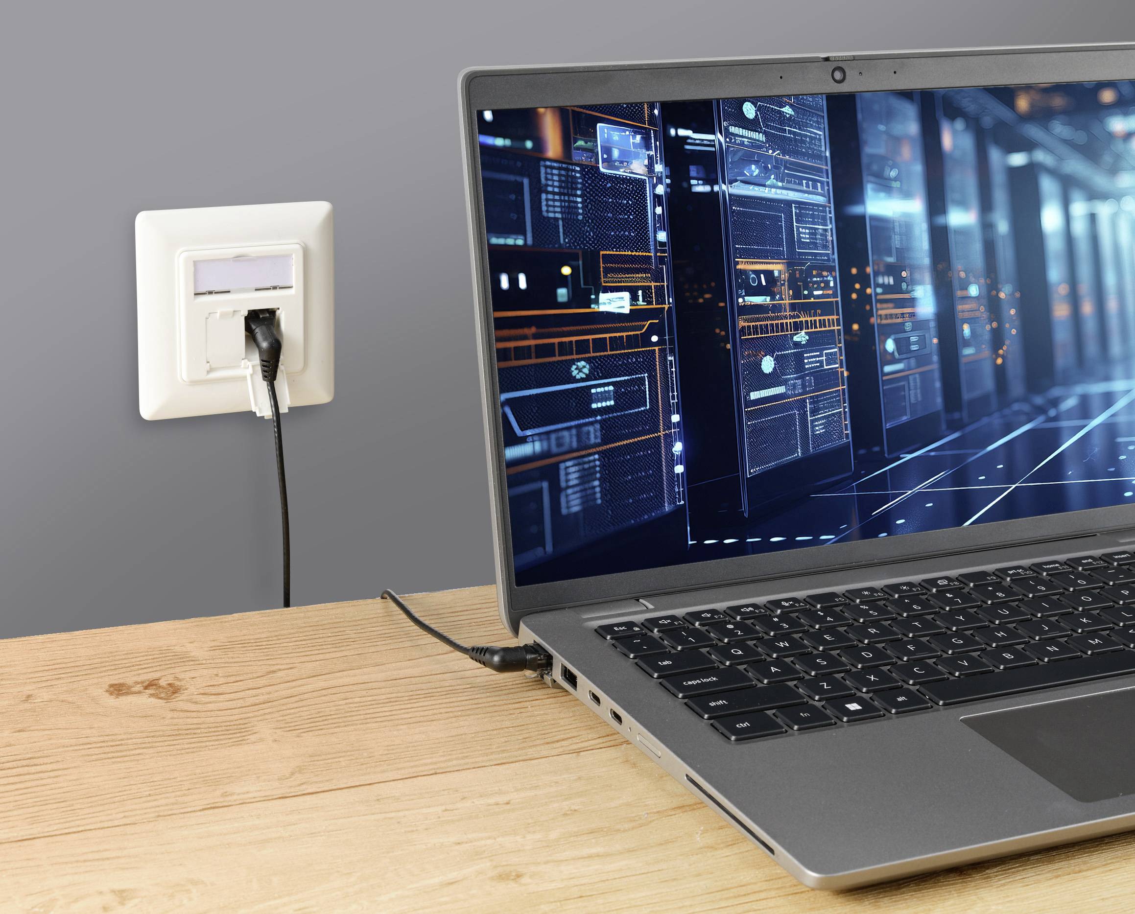 Ein Laptop auf einem Tisch zeigt eine technische Benutzeroberfläche, verbunden mit einer Steckdose an der Wand.