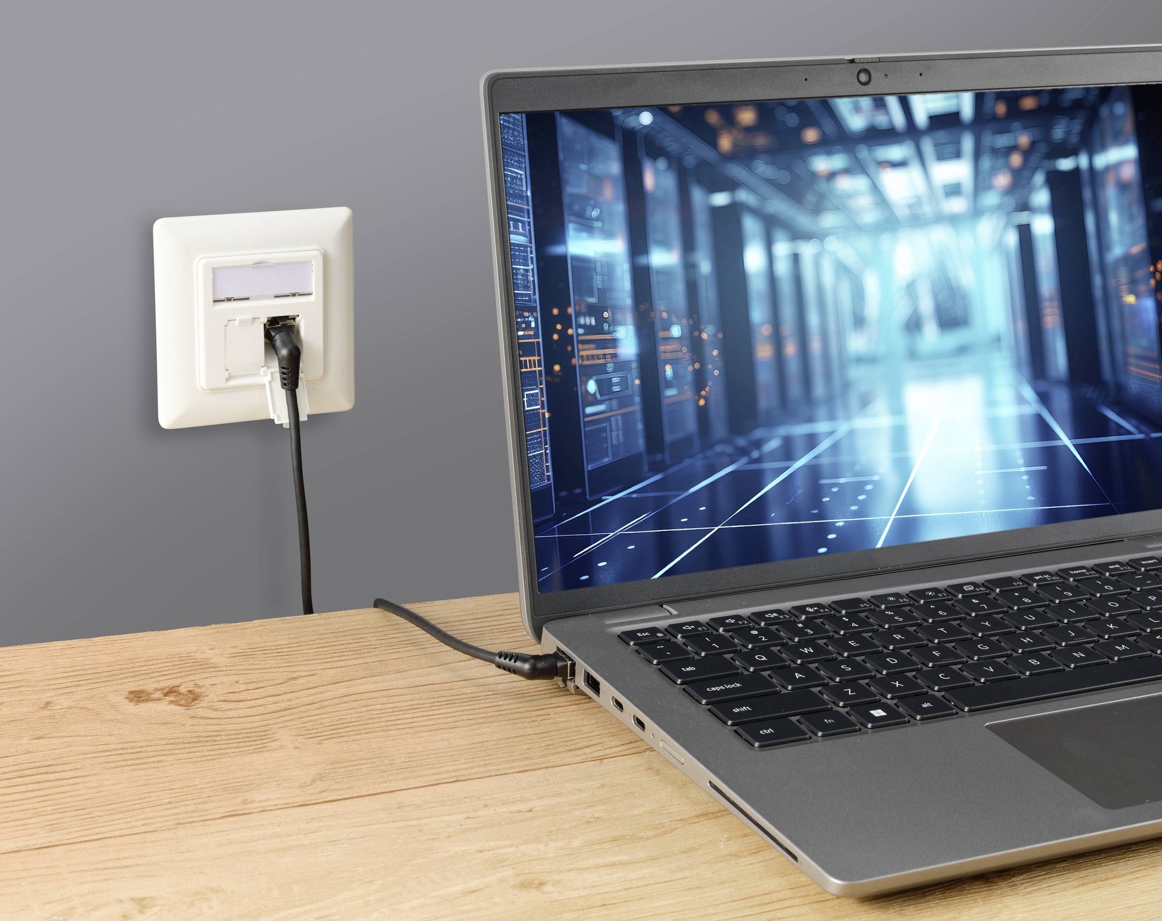 Laptop auf einem Tisch, verbunden mit einer Steckdose. Auf dem Bildschirm des Laptops ist ein digitales Serverraum-Render zu sehen.