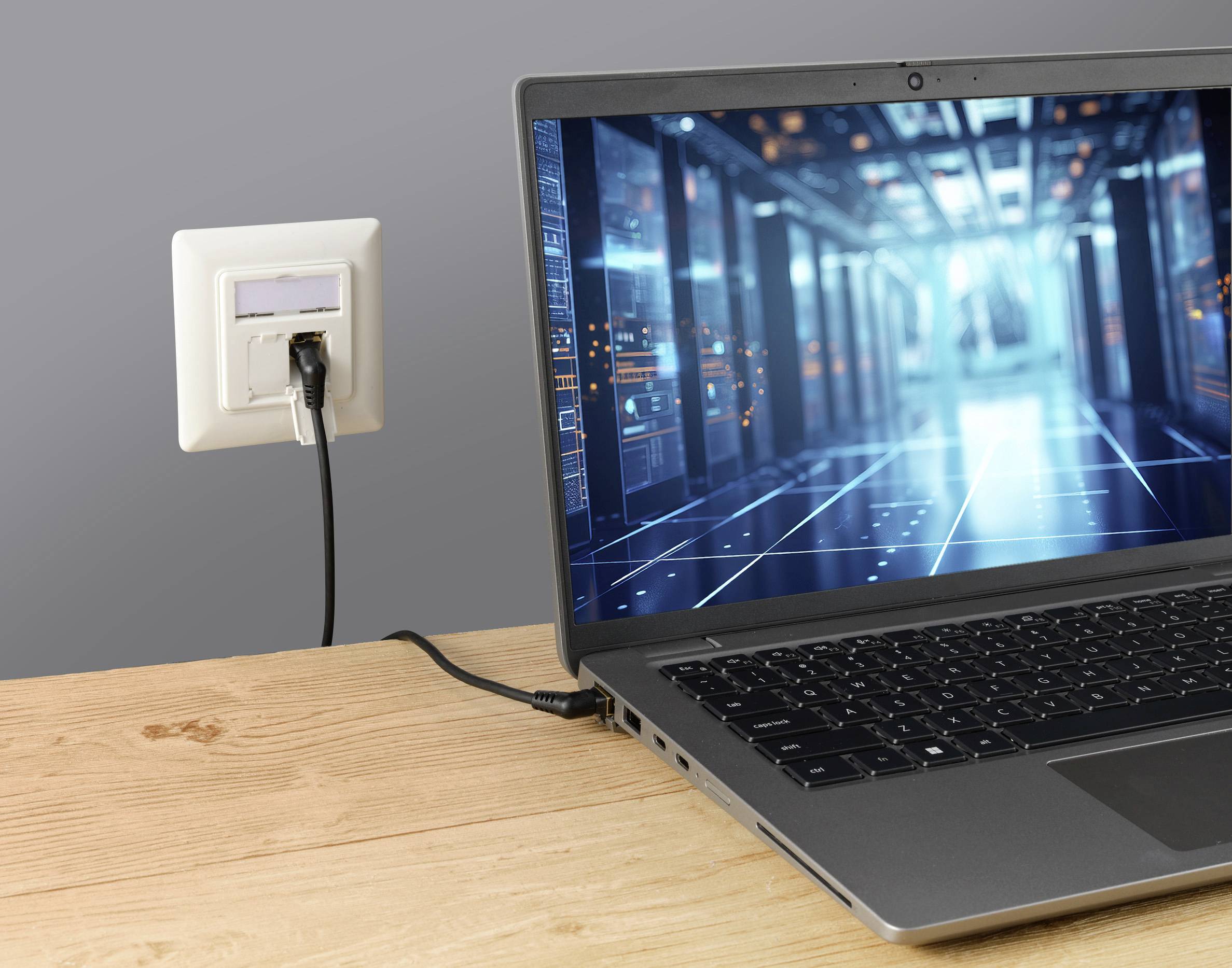 Laptop auf Holztisch zeigt ein digitales Datencenter auf dem Bildschirm, verbunden mit Netzwerkbuchse in der Wand.