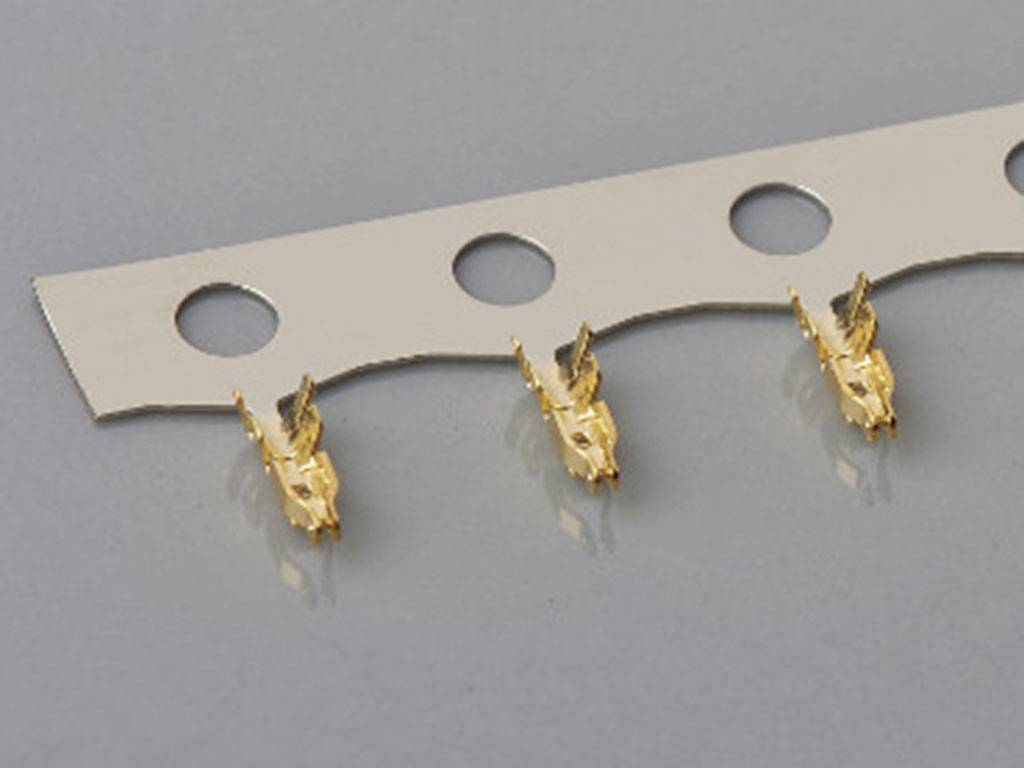 Drei kleine, goldene Metallteile sind gleichmäßig auf einem weißen Trägerband mit runden Löchern befestigt.