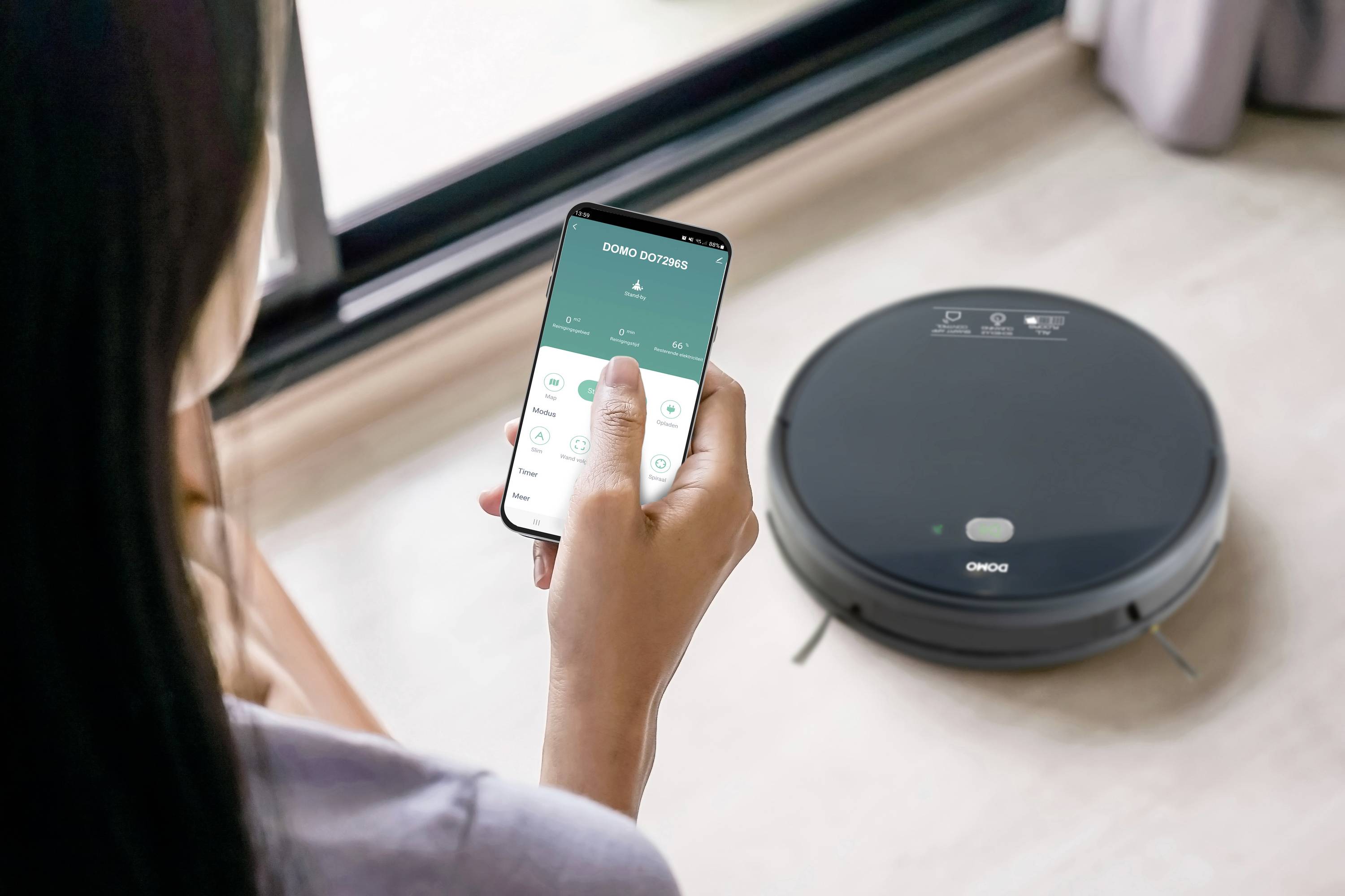 Eine Person steuert mit einem Smartphone einen Saugroboter. Der Roboter ist auf einem hellen Holzboden in der Nähe eines Fensters.