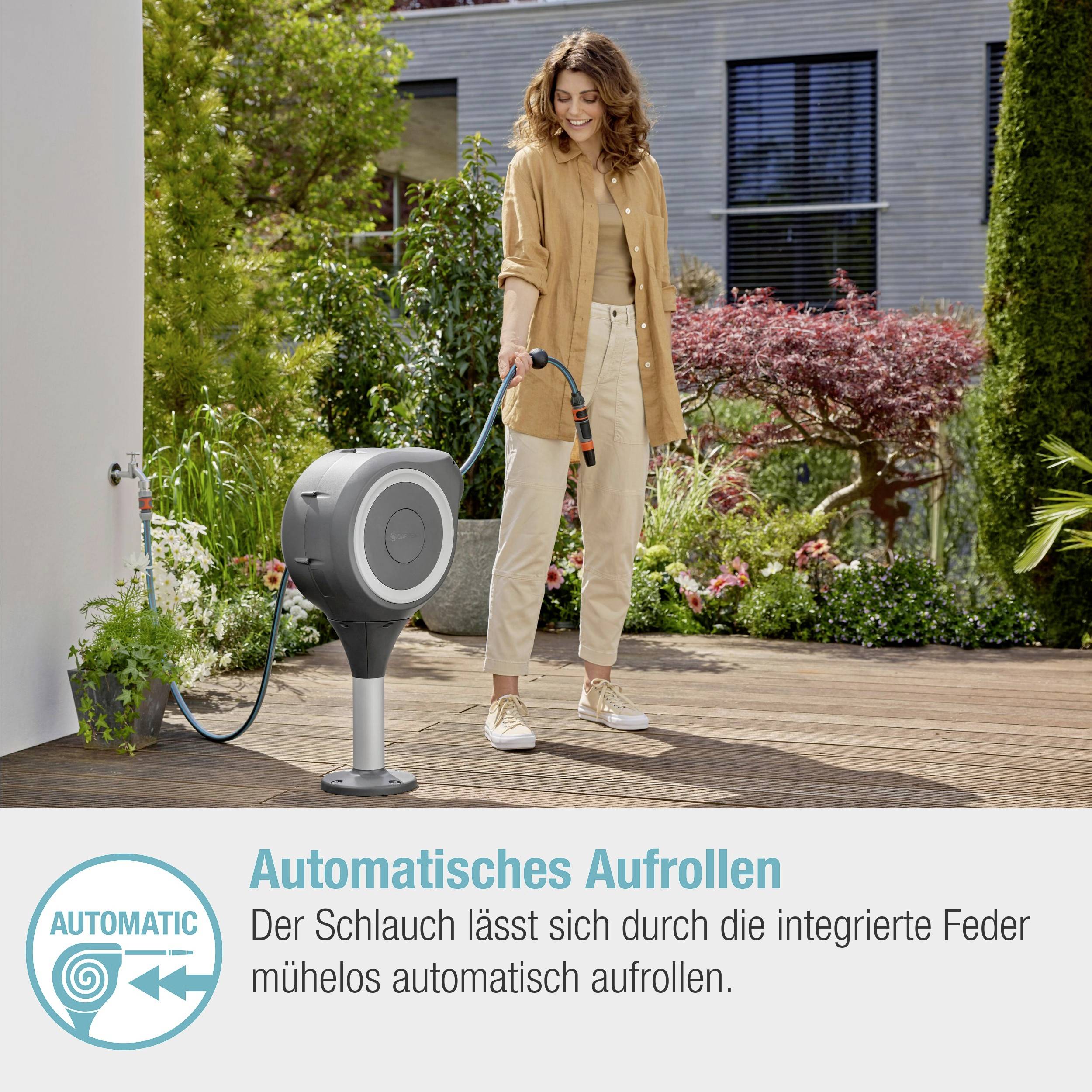 Eine Frau zieht einen Gartenschlauch aus einer automatischen Aufrollvorrichtung in einem Garten. Rechts unten steht: 'Der Schlauch lässt sich durch die integrierte Feder mühelos automatisch aufrollen'.