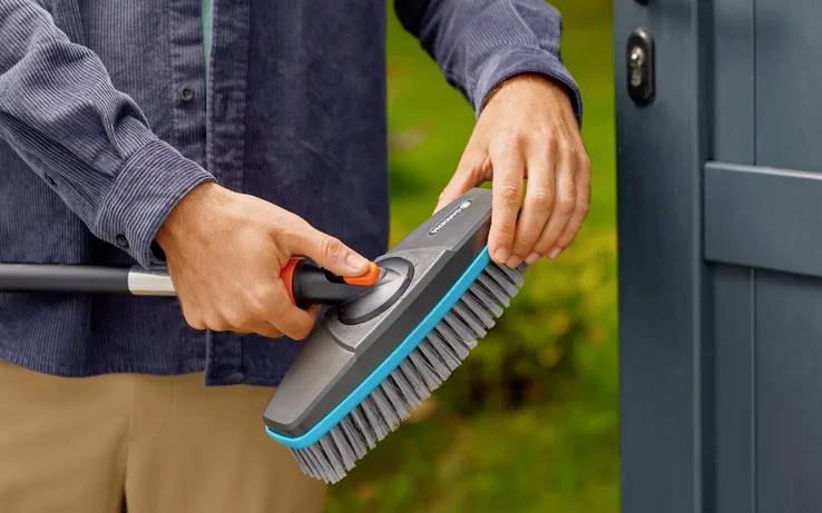 Eine Person benutzt eine Reinigungsbürste, um eine Oberfläche im Freien zu schrubben und sich dabei auf die Reinigungsaktion zu konzentrieren.