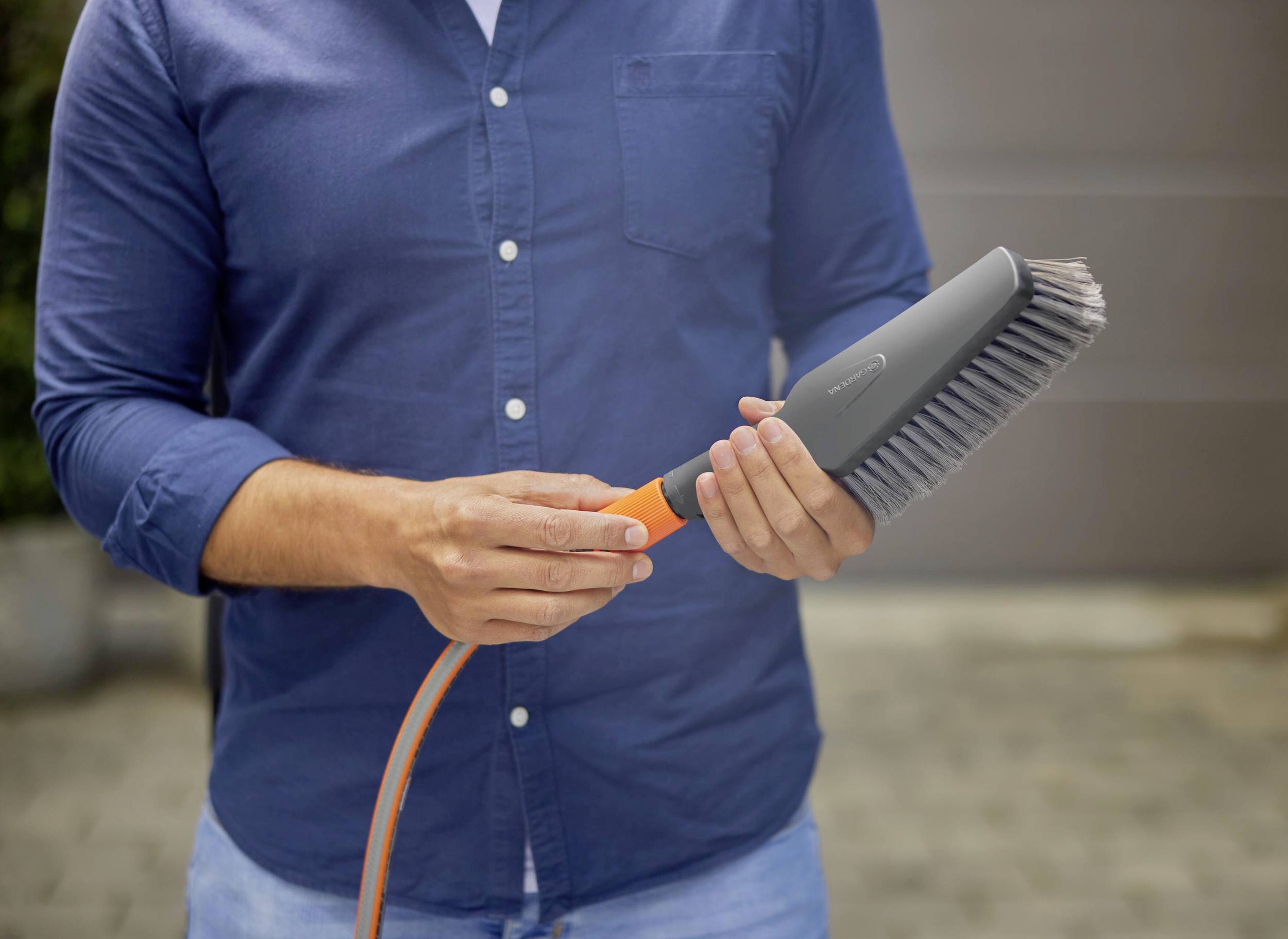 Eine Person hält eine Autowaschbürste mit einem Schlauchanschluss. Die Bürste hat Borsten und einen orangefarbenen Griff.