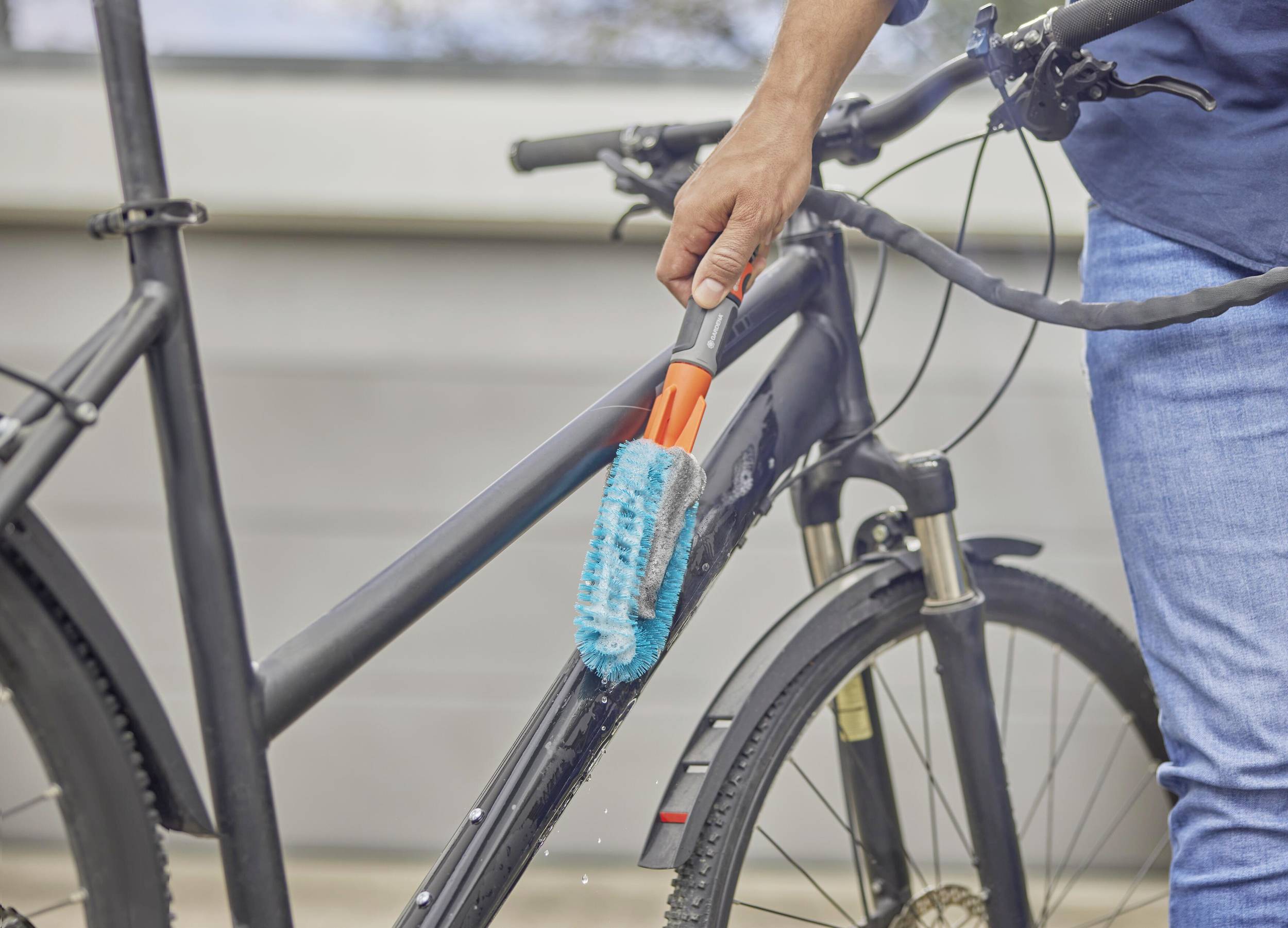 Eine Person reinigt mit einer blauen Bürste den Rahmen eines schwarzen Fahrrads im Freien.