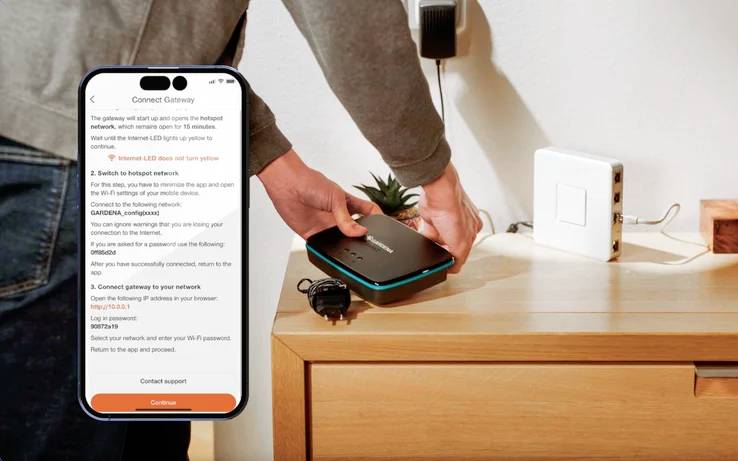 Person, die ein WLAN-Einrichtungsgerät neben einer Holzoberfläche hält und Einrichtungsanweisungen auf einem Smartphone auf dem Bildschirm befolgt.