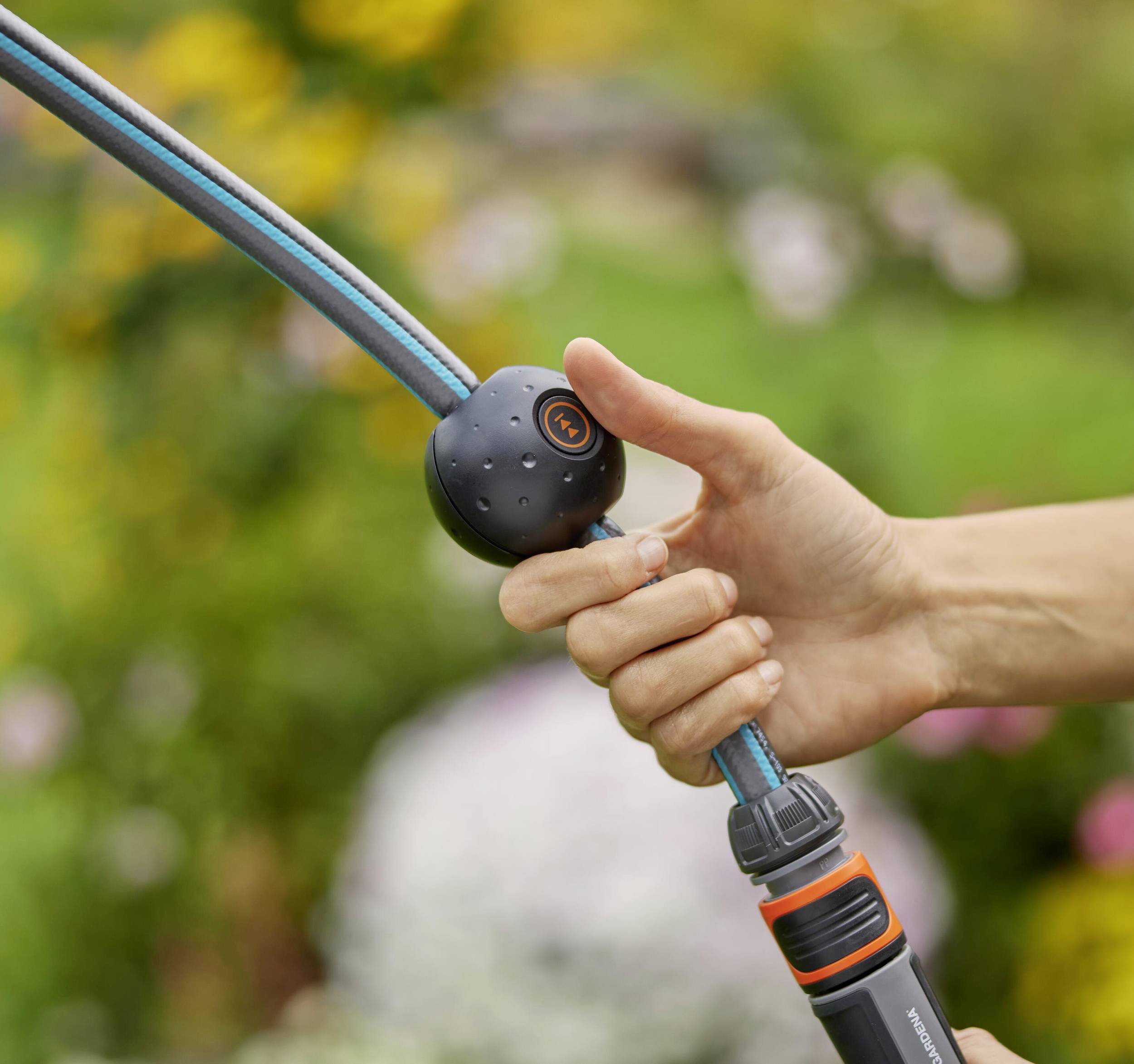 Eine Hand hält einen Gartenschlauch mit einem Sprühgerät, das in einem blühenden Garten verwendet wird.