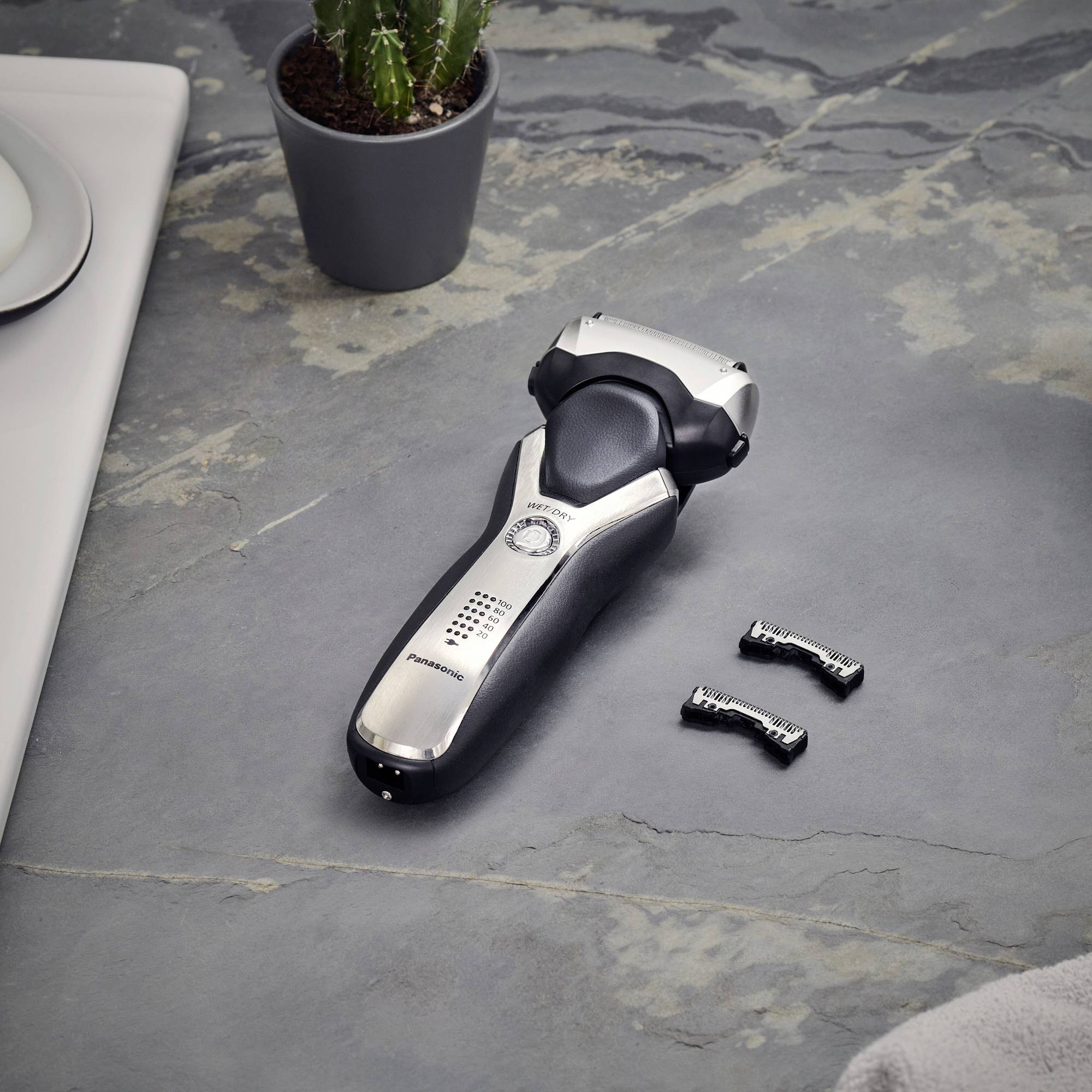 Elektrorasierer auf grauem Badetisch neben einem Kaktus und zwei Ersatzklingen.