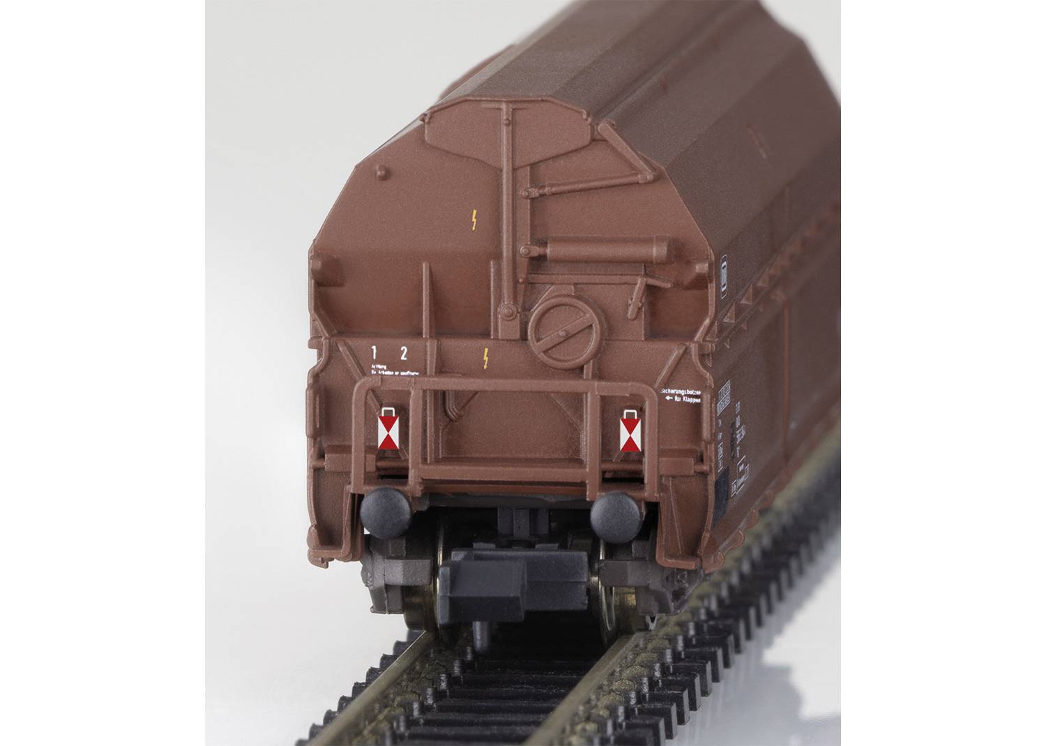 Ein Modellbahn-Güterwagen auf Gleisen, braun lackiert, mit weißen Beschriftungen und roten Markierungen.