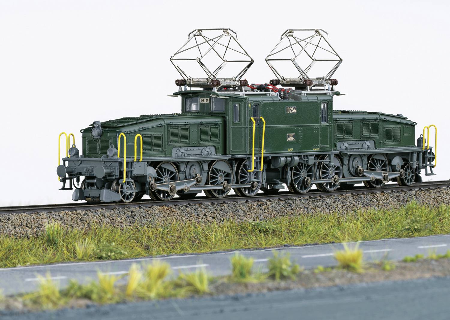 Ein grünes, detailliertes Modell einer alten Elektrolokomotive mit mehreren Pantografen steht auf einem Gleis, umgeben von Gras.