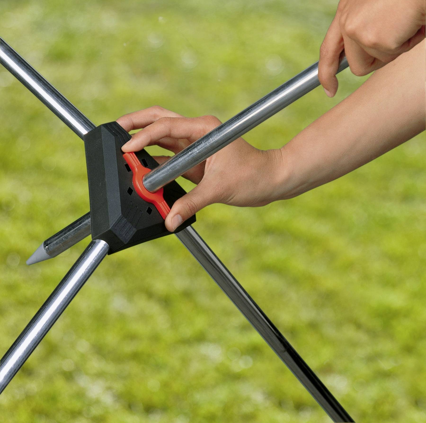 Eine Person verwendet ein rotes Werkzeug, um den Winkel eines Metalldreifußes auf Gras einzustellen und konzentriert sich dabei auf den Mechanismus zum Sichern seiner Beine.