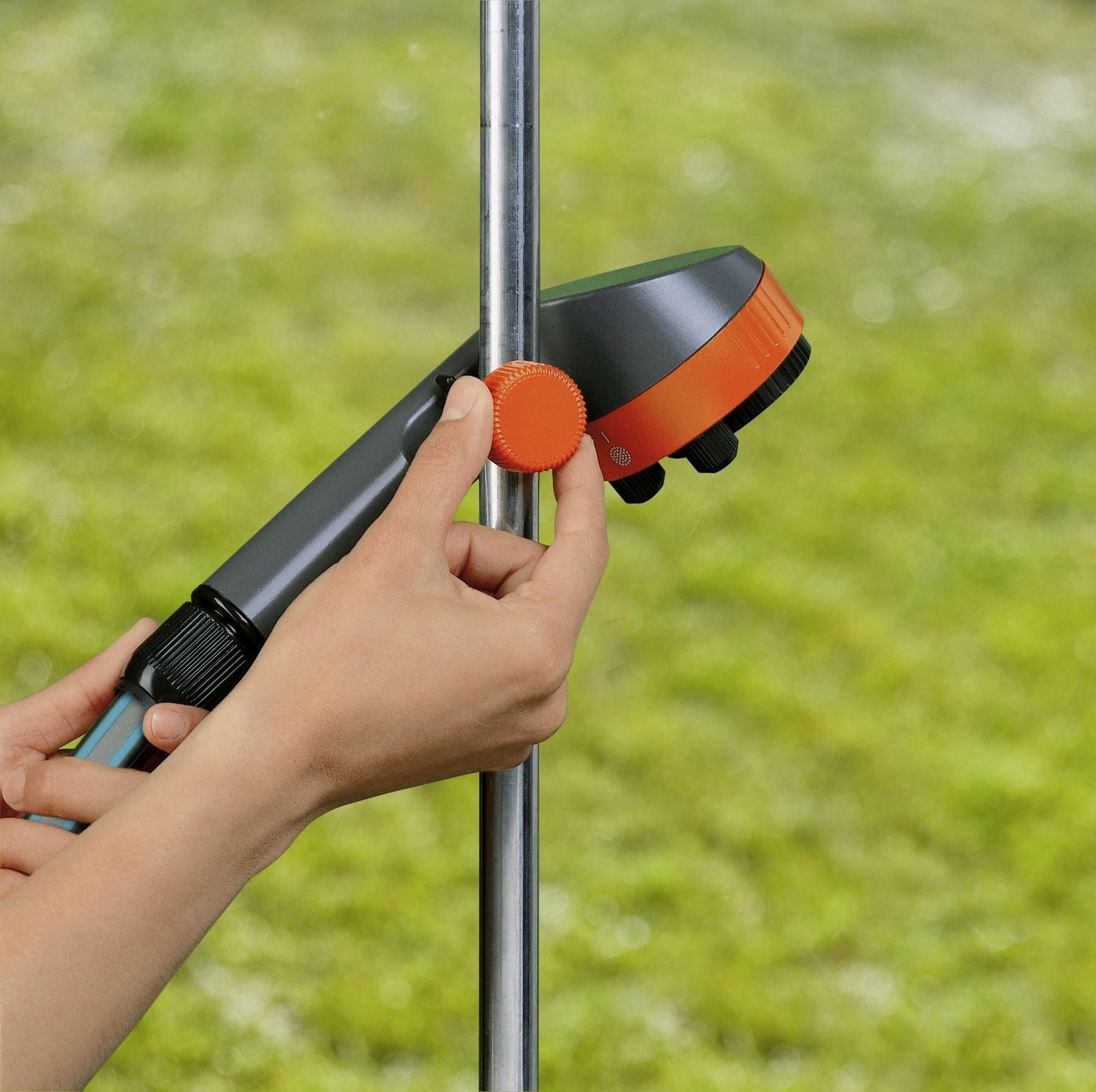 Eine Person justiert eine Klemme an einem vertikalen Metallpfosten im Freien und hält dabei ein Werkzeug mit einer orangefarbenen Skala und einem Schlauchansatz, vor einem Hintergrund aus Gras.