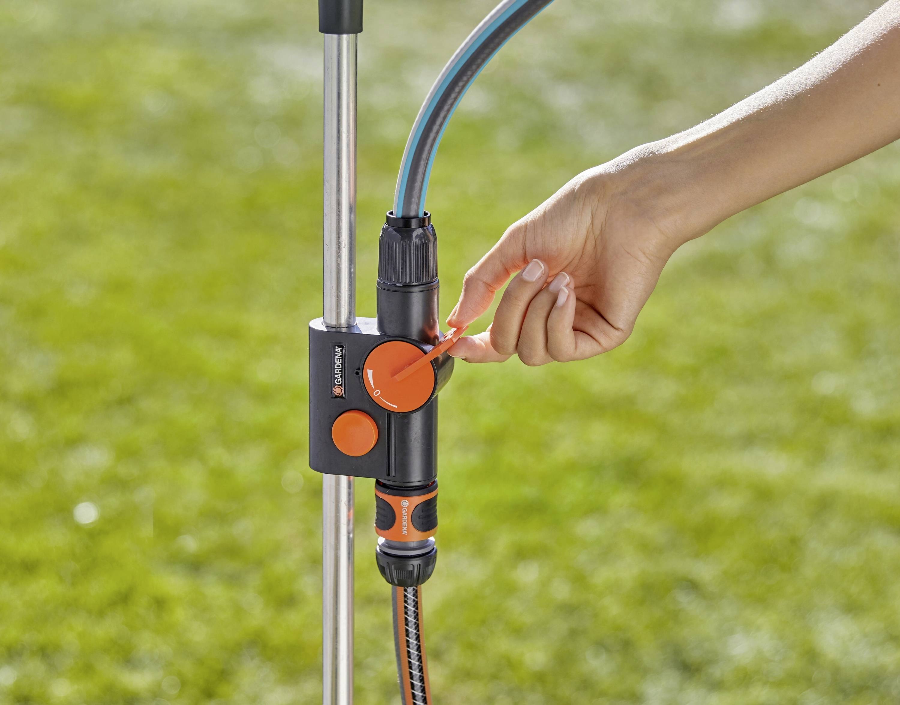 Eine Hand justiert ein Kontrollventil an einem Gartenwasserschlauch-Setup, mit einem grünen Rasen im Hintergrund.