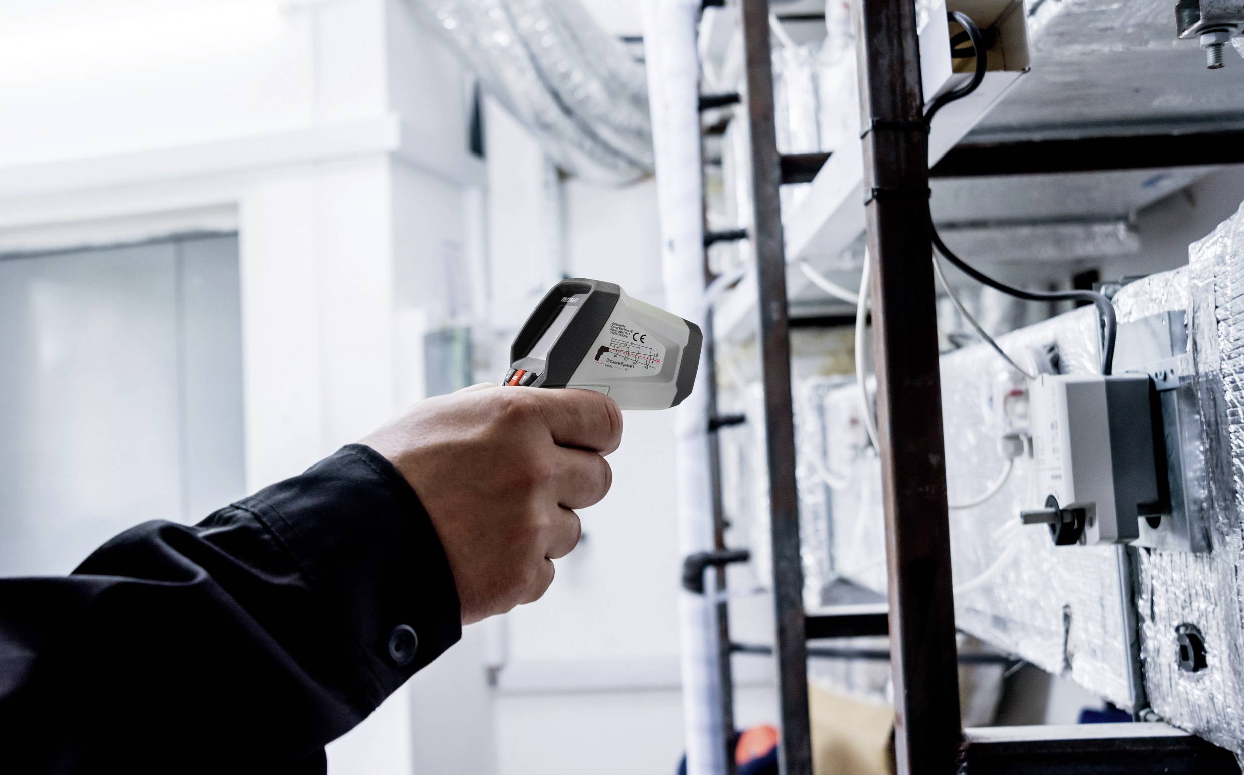 Eine Person misst die Temperatur einer Heizungsanlage mit einem Infrarot-Thermometer.