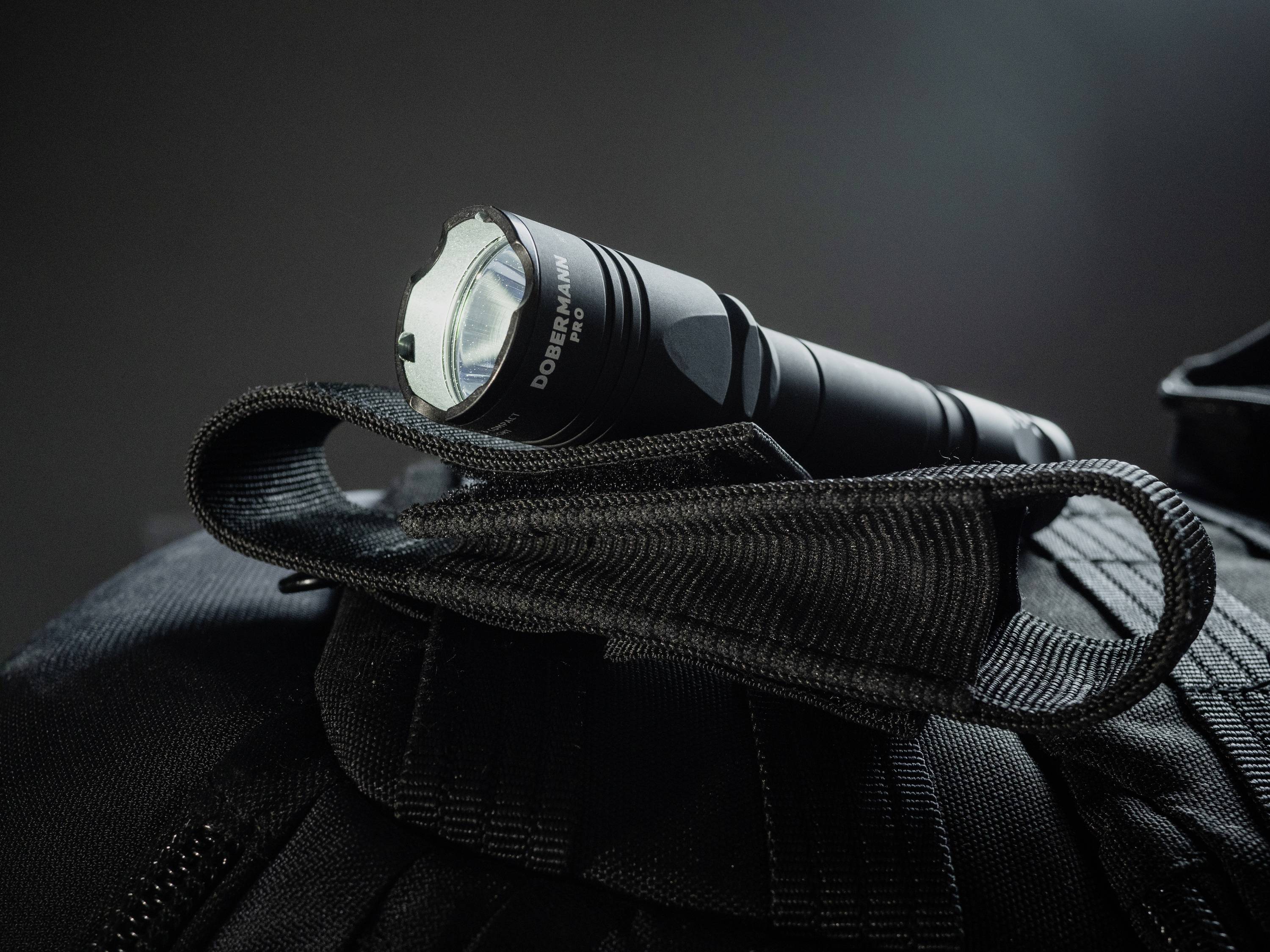 Eine schwarze Taschenlampe liegt auf einer schwarzen Tasche. Der Fokus liegt auf der Taschenlampe, die in einer Schlaufe befestigt ist.