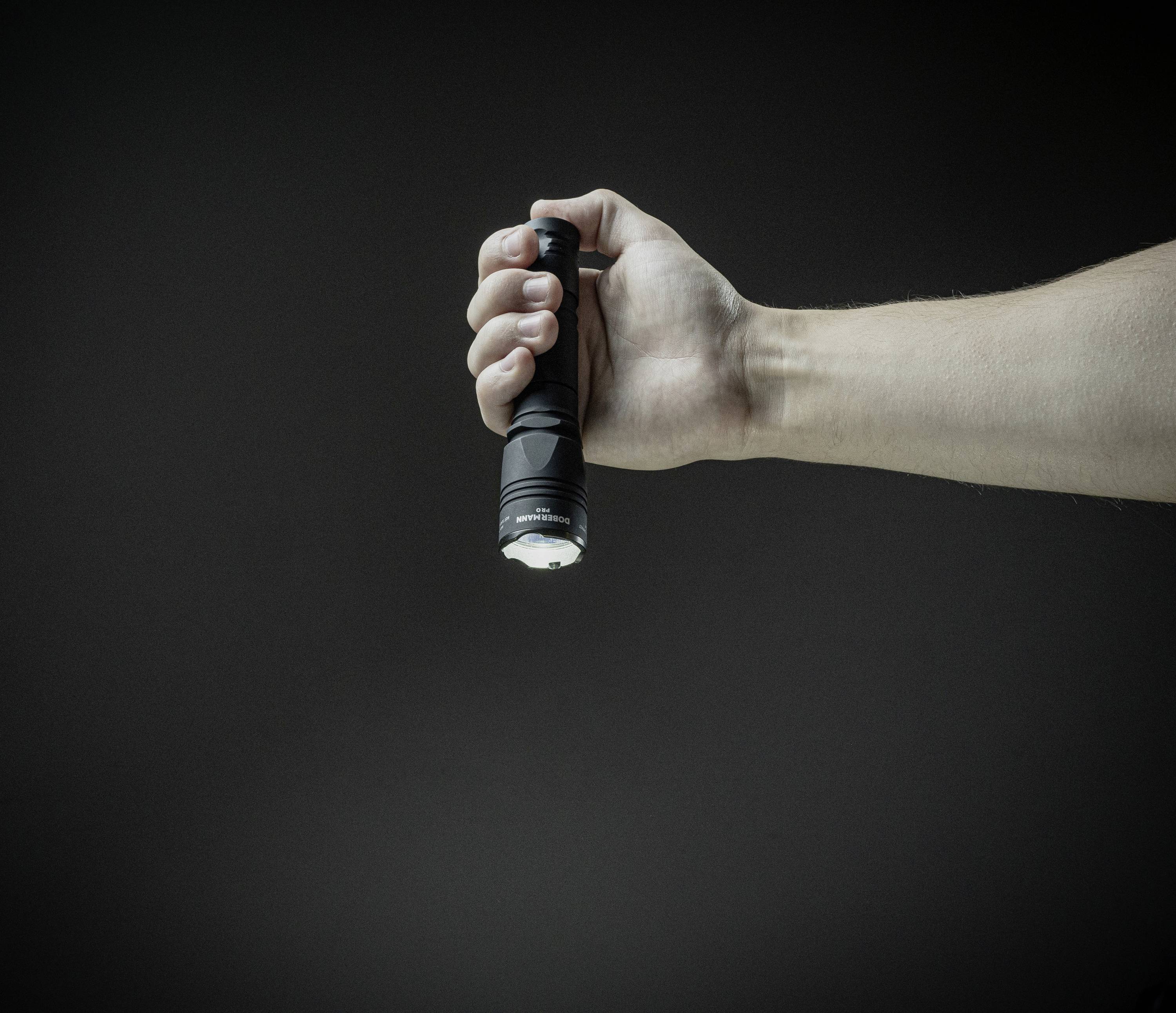 Eine Hand hält eine schwarze Taschenlampe in einem dunklen Raum, die nach unten leuchtet.