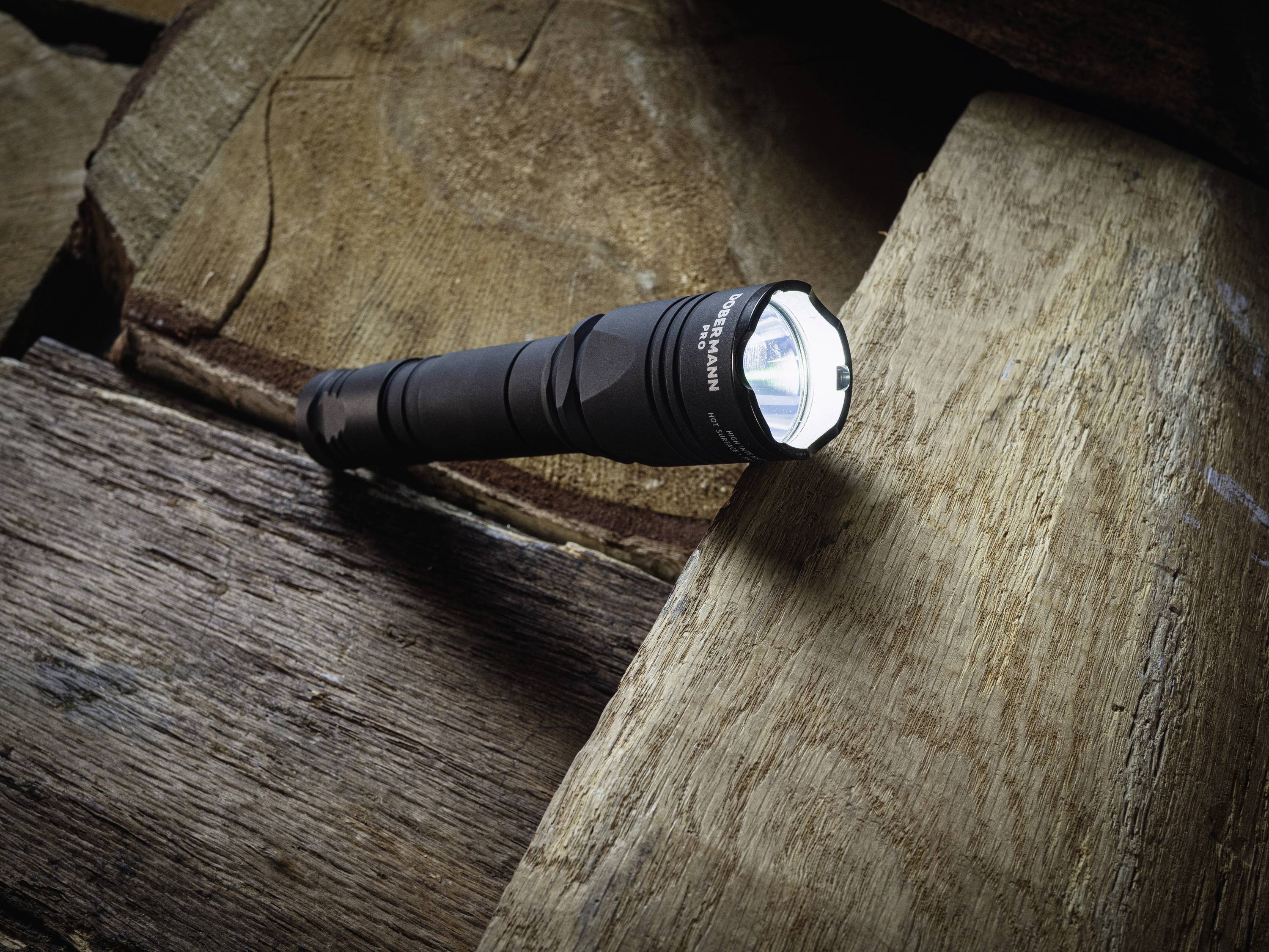 Taschenlampe liegt auf Holzoberfläche. Sie leuchtet und hebt sich durch ihren Lichtstrahl von der Struktur des Holzes ab.