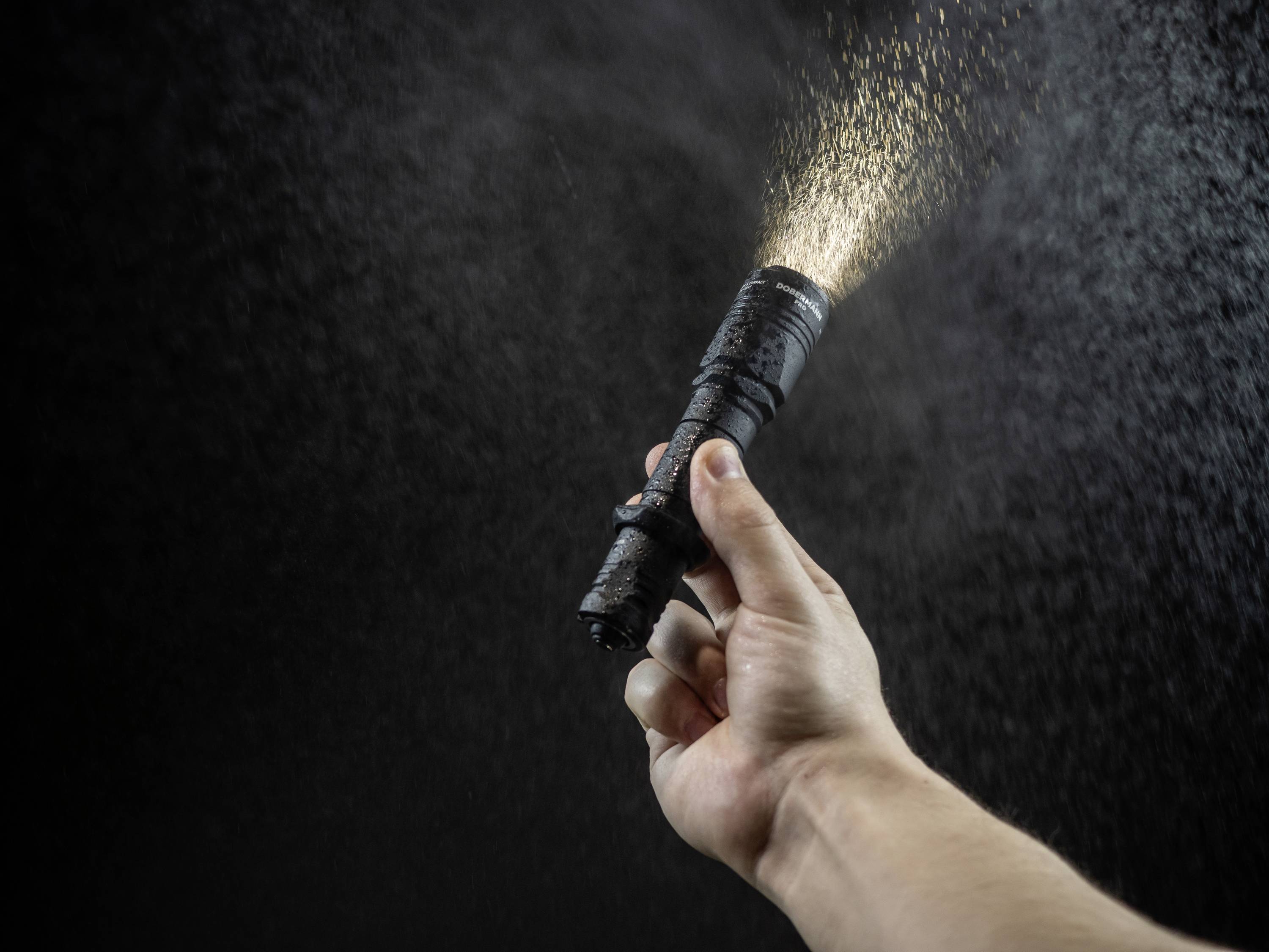 Eine Hand hält eine Taschenlampe, aus der ein Lichtstrahl im dunklen Raum leuchtet. Feiner Staub oder Partikel schweben im Licht.