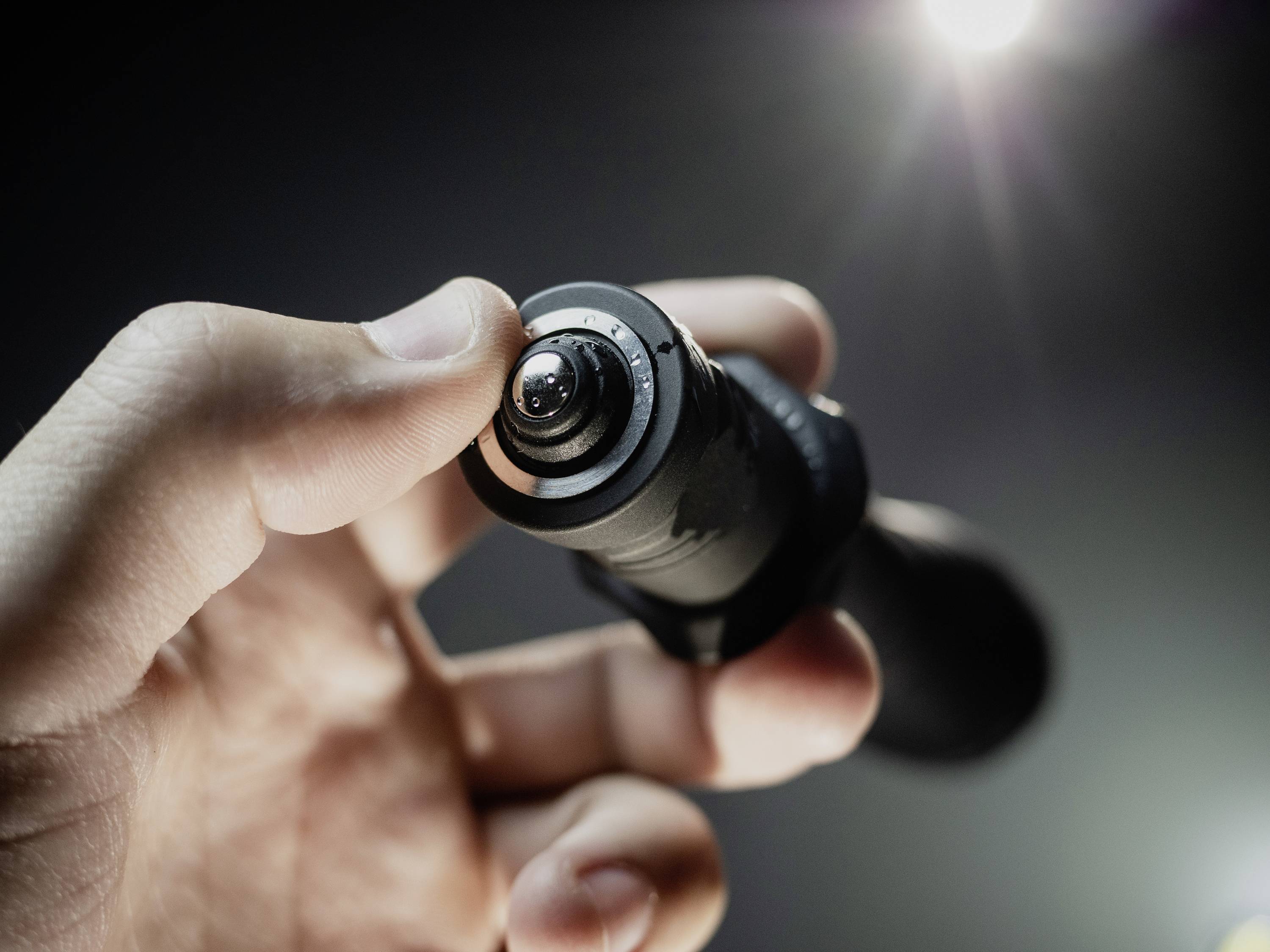 Eine Hand hält eine Nahaufnahme eines Kameraobjektivs oder ähnlichen optischen Geräts. Es ist bei schwachem Licht beleuchtet.