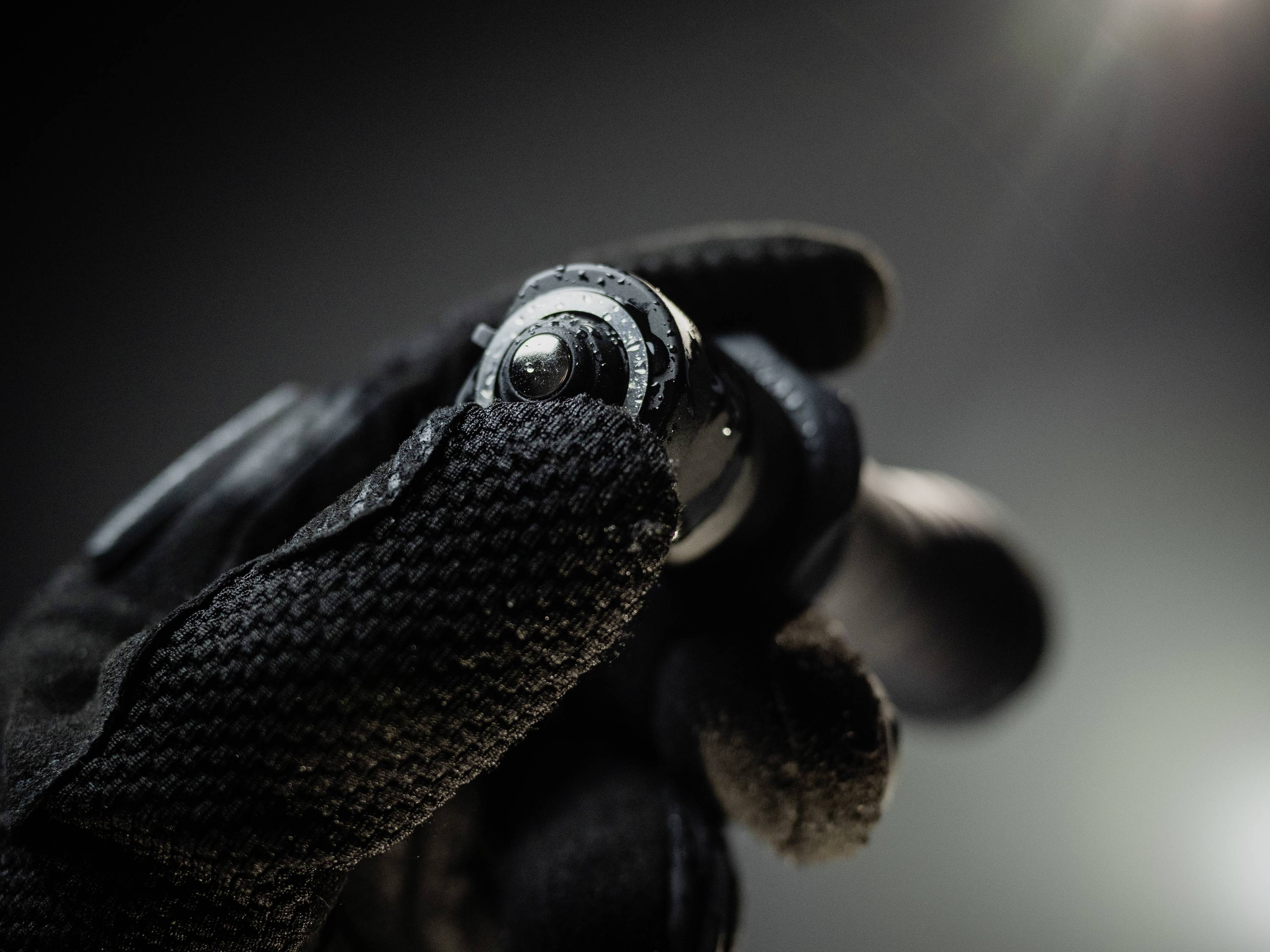 Eine Hand in einem schwarzen Handschuh hält eine kleine Taschenlampe. Die Umgebung ist dunkel und die Lampe ist eingeschaltet.