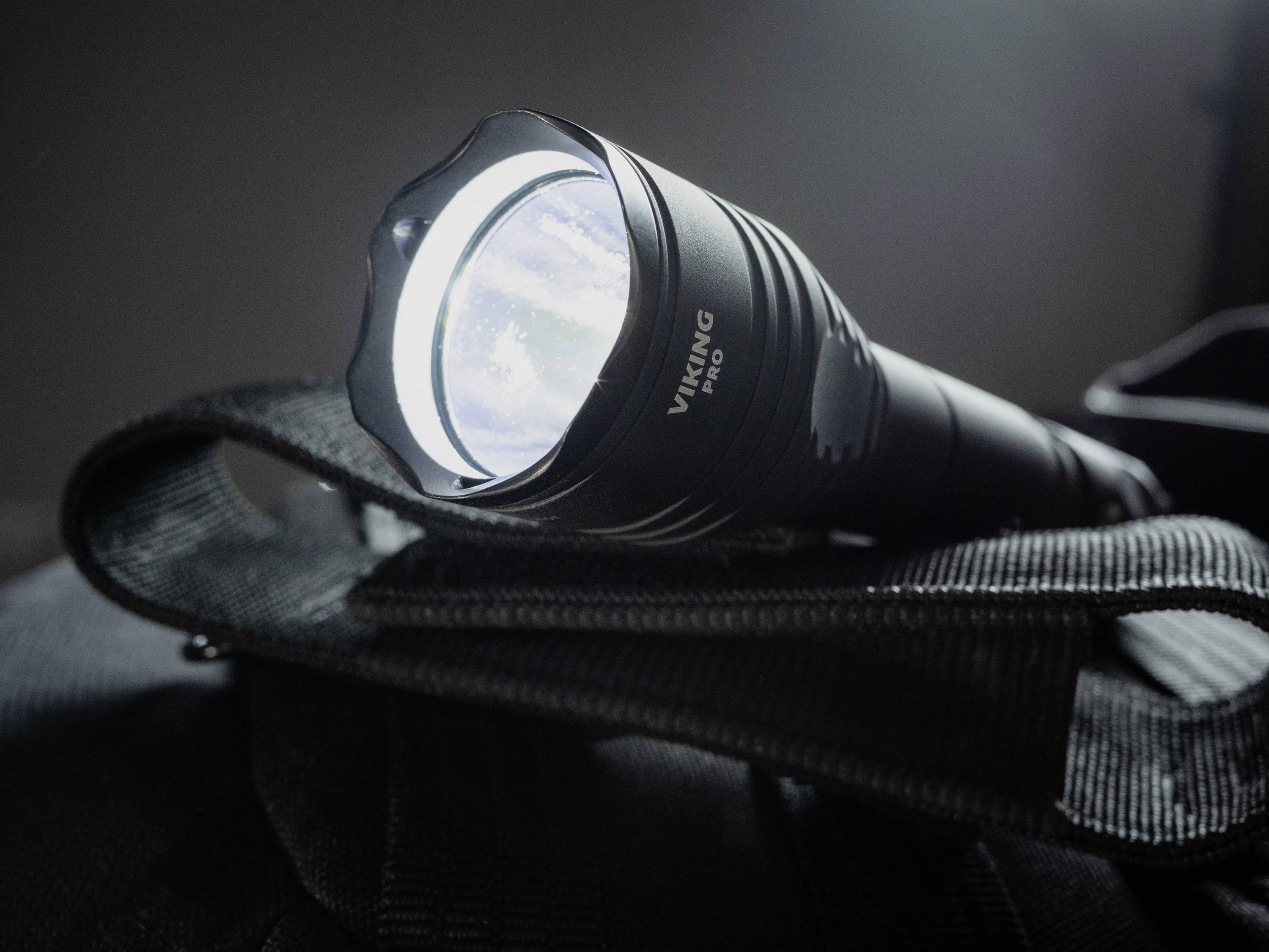 Eine eingeschaltete Taschenlampe liegt auf einer schwarzen Tasche. Sie leuchtet hell und hebt sich vom dunklen Hintergrund ab.