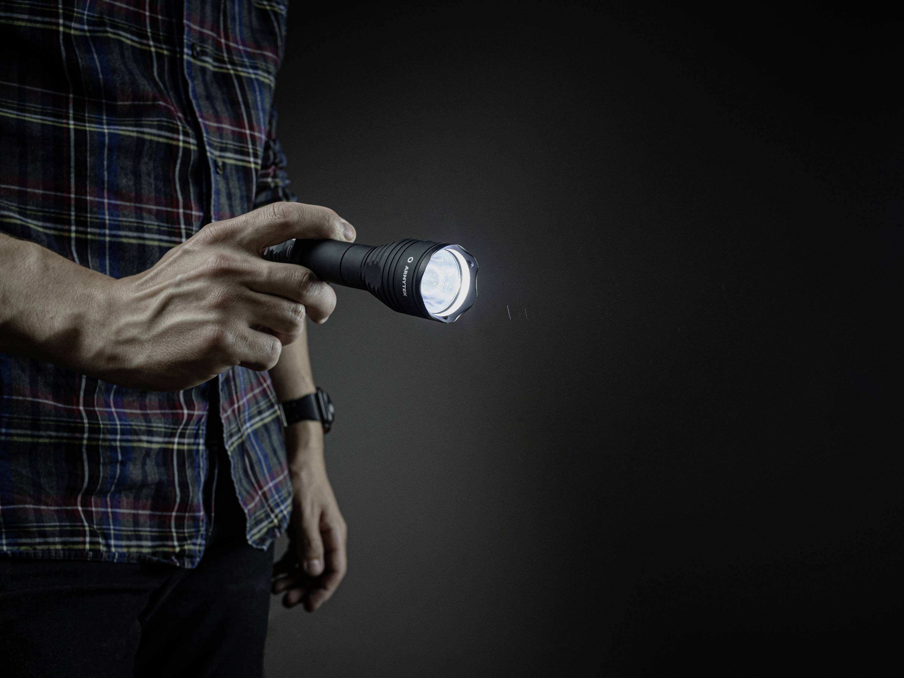 Eine Person hält eine leuchtende Taschenlampe in dunkel beleuchteter Umgebung. Der Lichtstrahl richtet sich nach vorne.