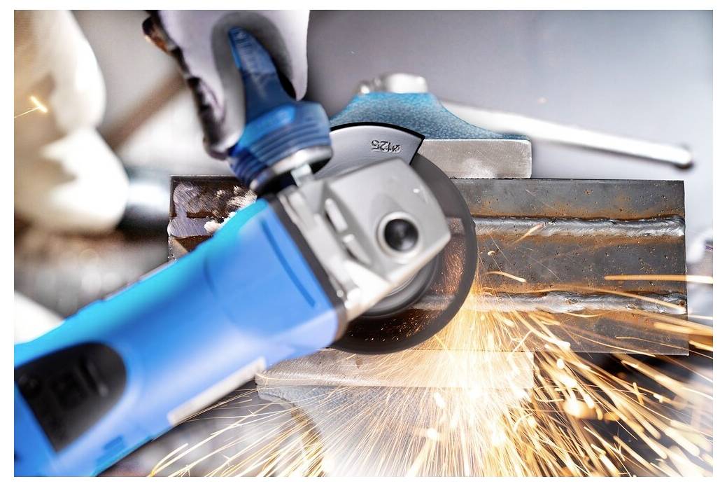 Eine Person verwendet einen blauen Winkelschleiffer auf einer Metalloberfläche und erzeugt dabei helle orange Funken.