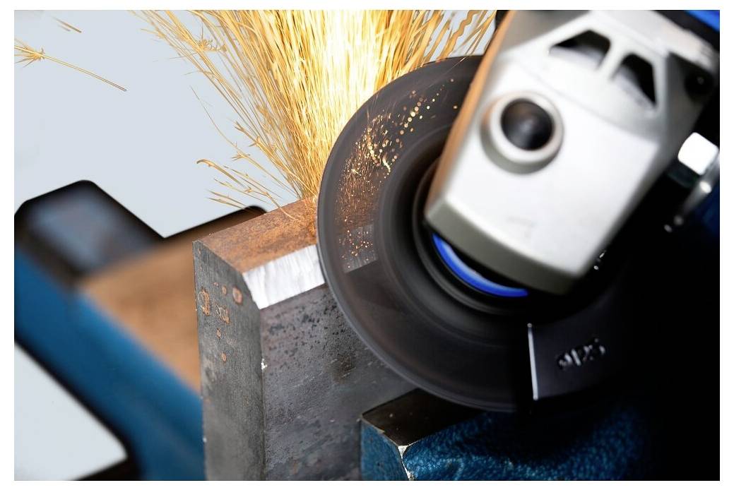 Eine Nahaufnahme einer Metallschleifmaschine in Aktion, die einen Metallblock schleifen, mit fliegenden Funken, wobei industrielle Arbeit und Werkzeugpräzision gezeigt werden.