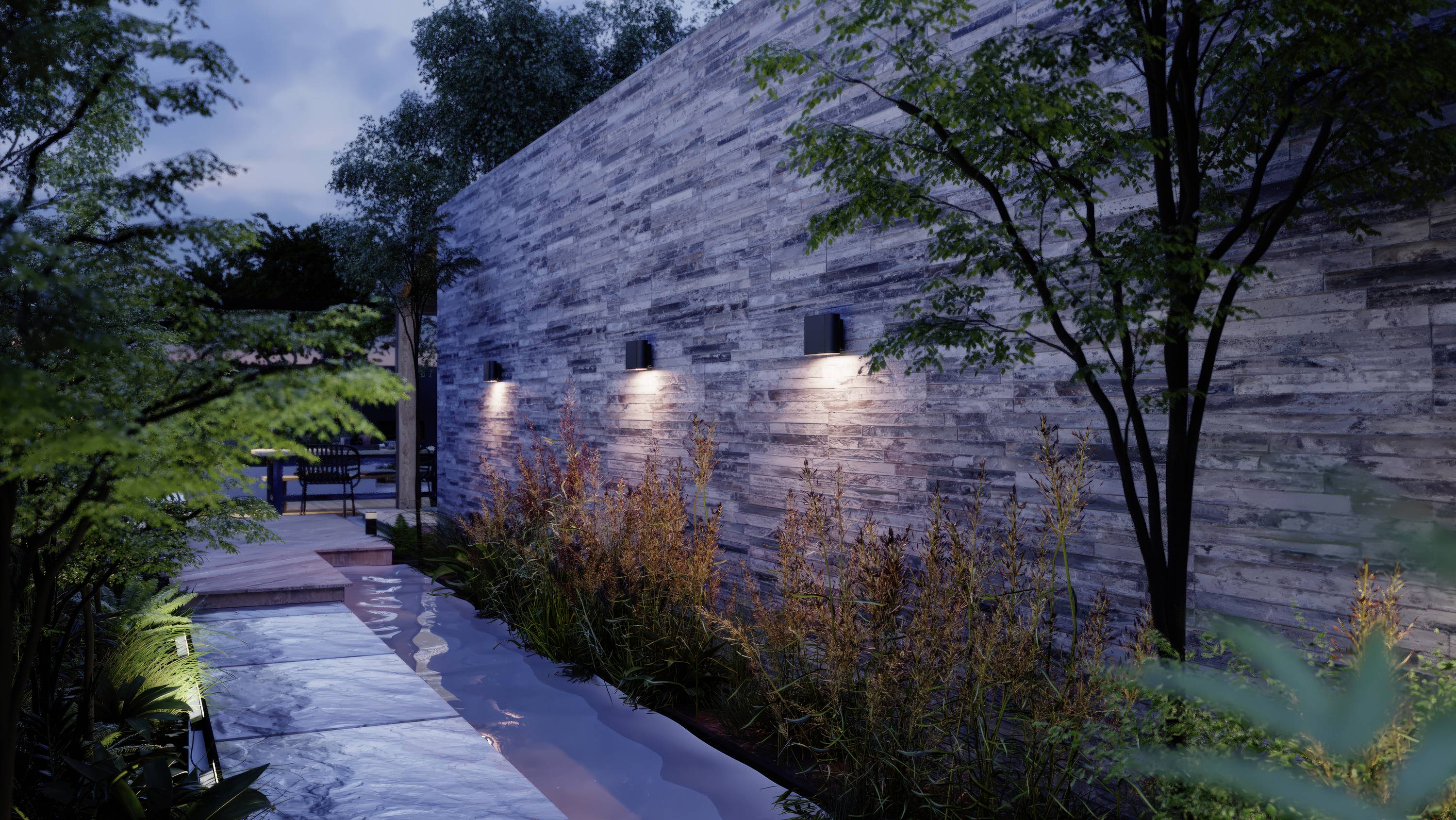 Pfad mit Wasserelement und Bäumen entlang einer beleuchteten Steinmauer in einem modernen Garten bei Dämmerung.