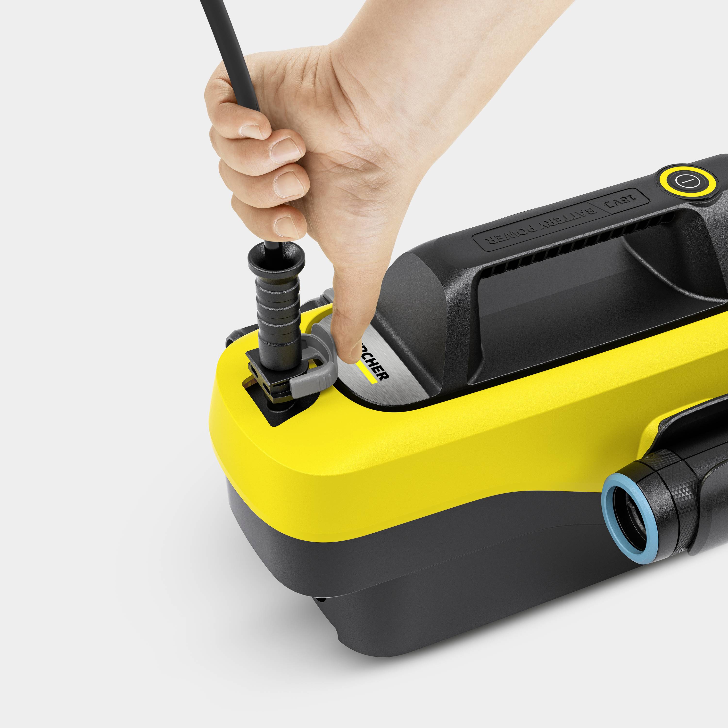 Eine Hand verbindet einen Schlauch mit einem gelben Hochdruckreiniger, der auf einer flachen Oberfläche steht.