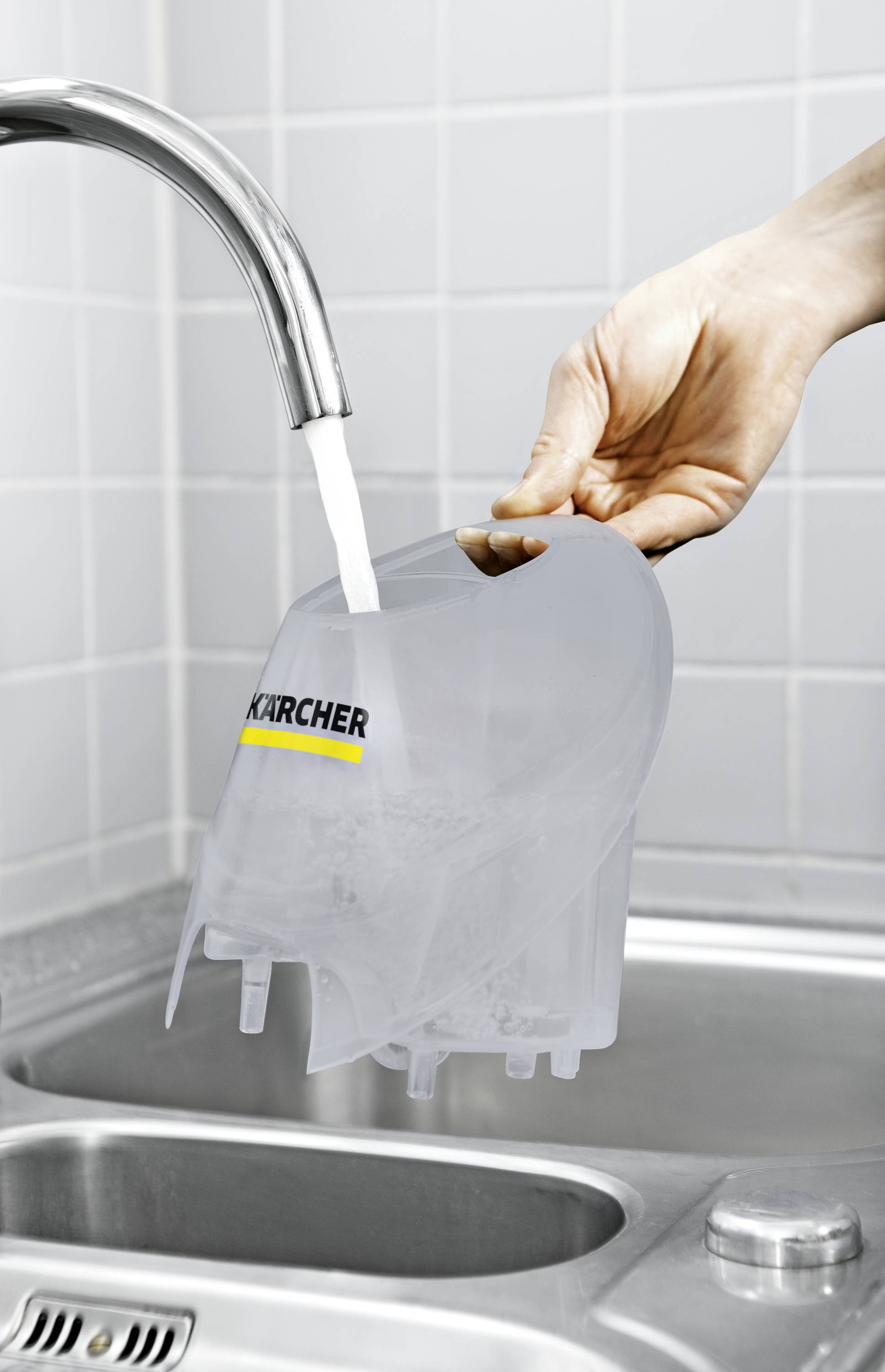 Eine Hand hält einen grauen Wassertank unter fließendem Wasser aus einem Wasserhahn in einer Küchenspüle.