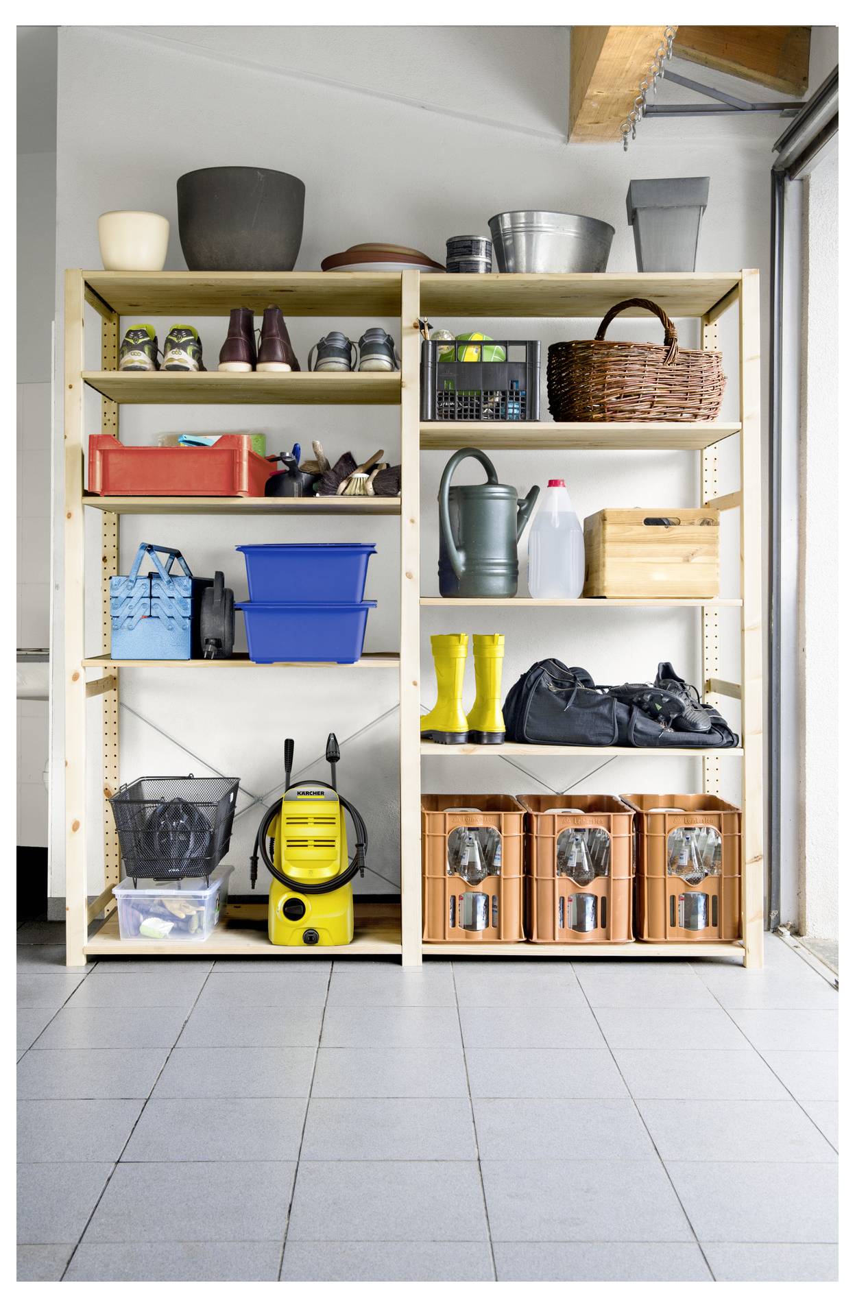 Hölzerne Regale in einer Garage halten Gartengeräte, Stiefel, Aufbewahrungskisten und Reinigungsutensilien. Leuchtend gelbe Stiefel und ein Staubsauger sind zu sehen.