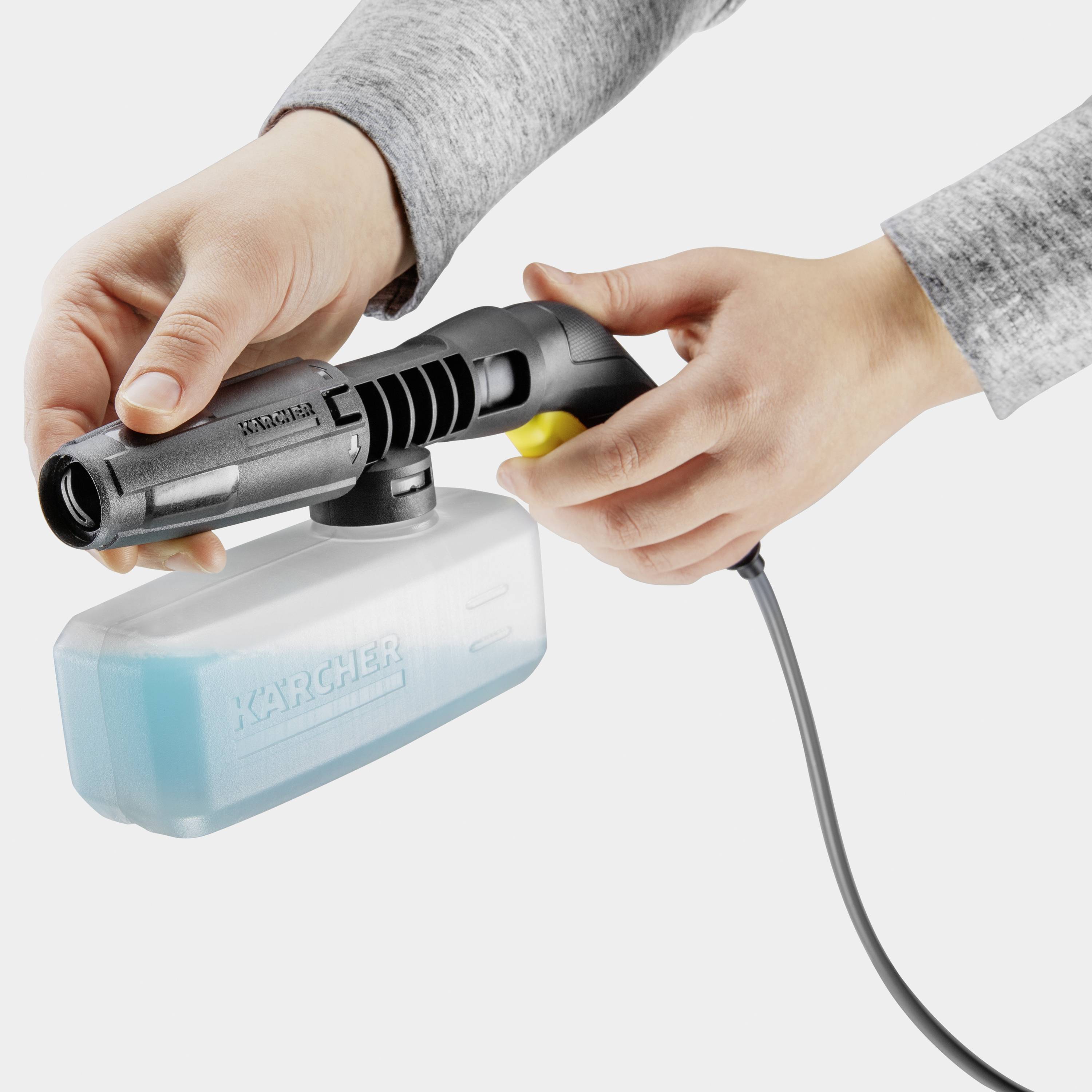 Person hält eine Reinigungsdüse mit einem blauen Flüssigkeitsbehälter. Werkzeug von Kärcher mit Kabel zur Stromversorgung.