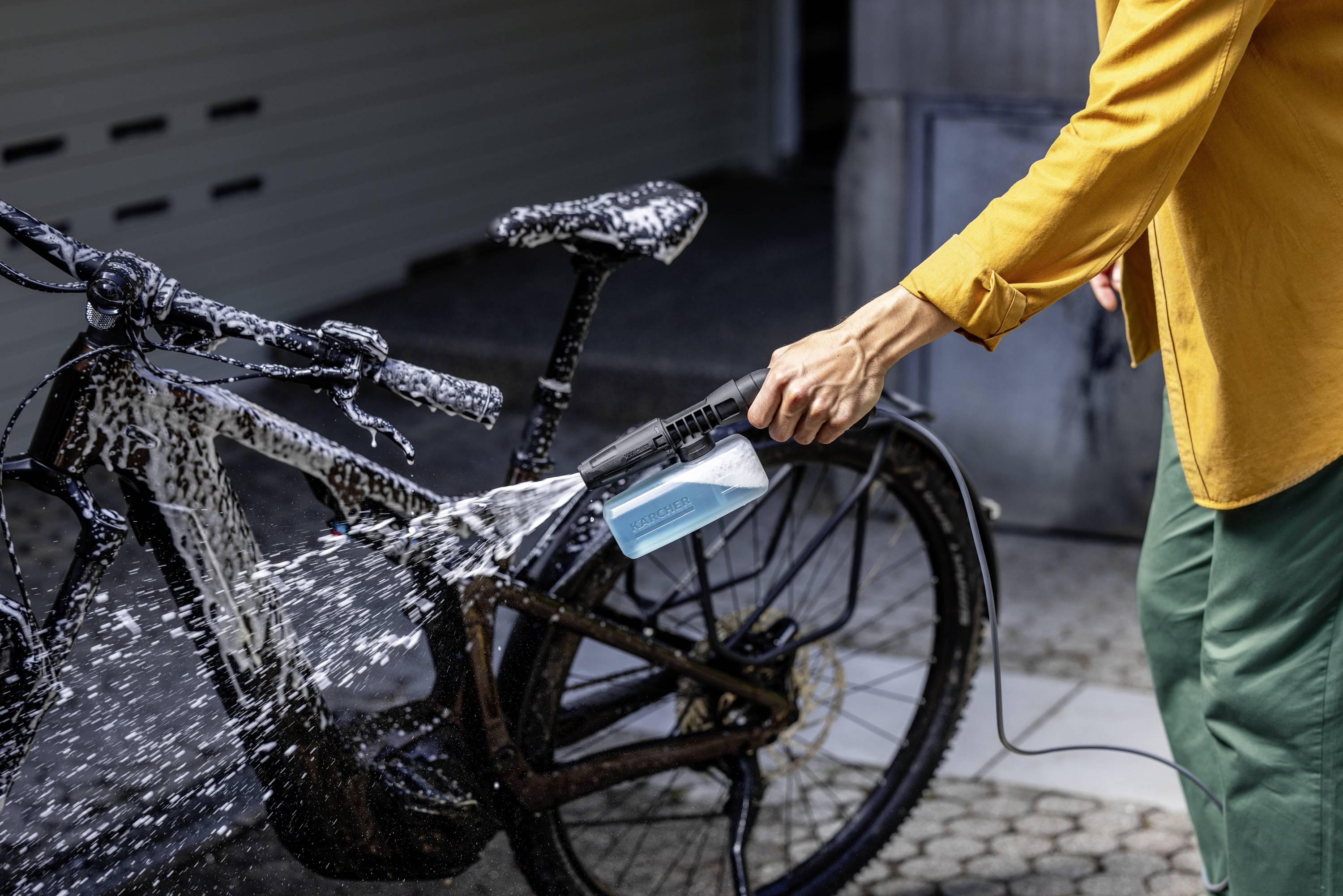 Eine Person wäscht ein Fahrrad mit einem Hochdruckreiniger, das Fahrrad ist mit Seifenwasser bedeckt.